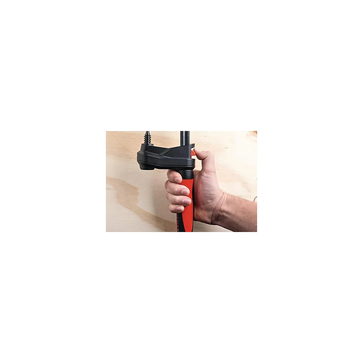 Une personne tient un serre-joint noir avec une poignée rouge. Le bouton de déverrouillage rouge est enfoncé avec un doigt.