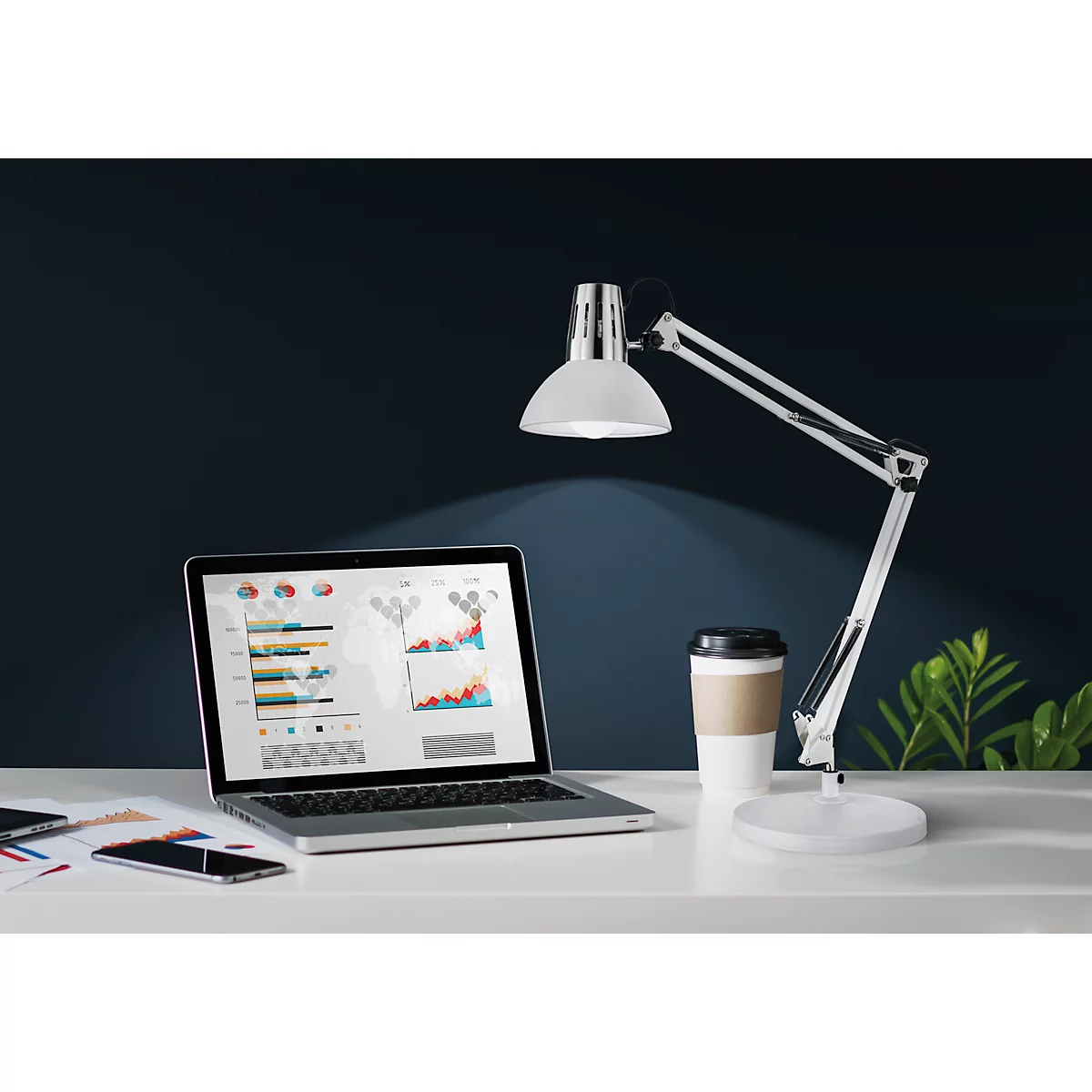 Desk with laptop, lamp and coffee cup. Charts are visible on the screen.