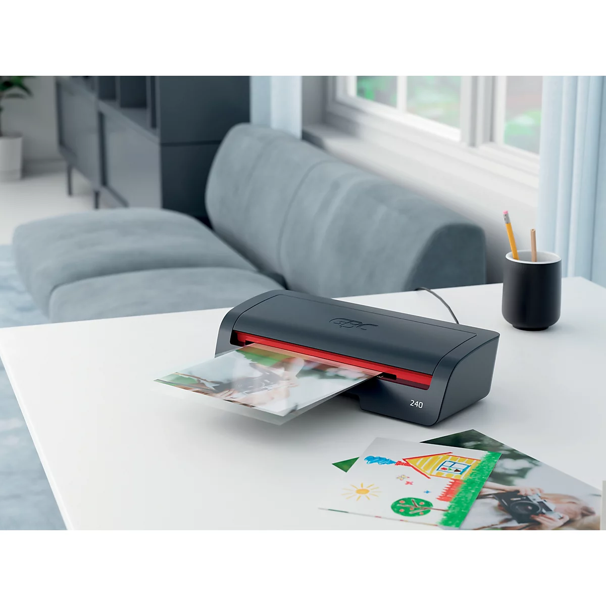 Une plastifieuse sur une table plastifiant une photo. En arrière-plan, un canapé, une fenêtre et d'autres photos.