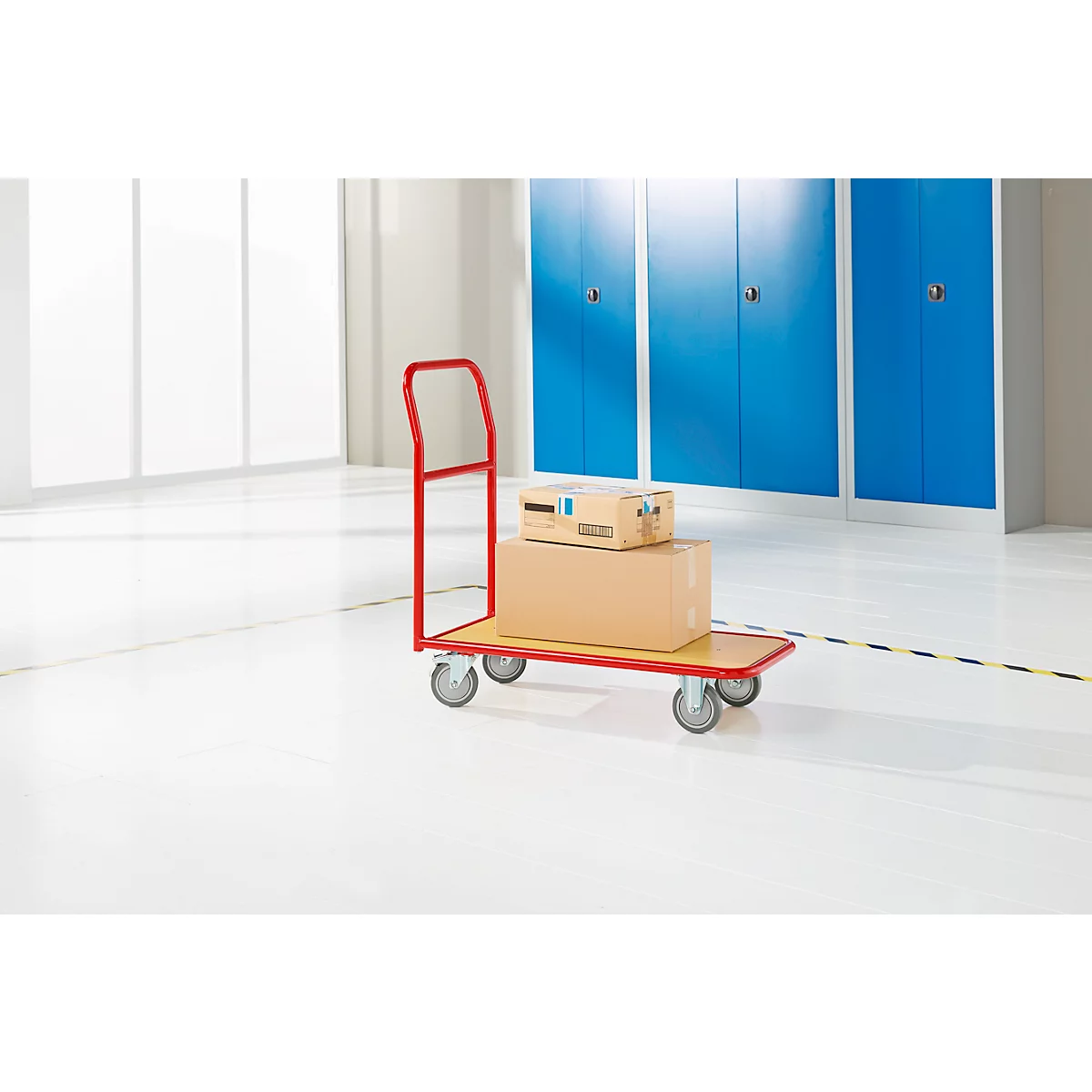 A red cart with packages stands in front of blue cabinets. The floor is white.