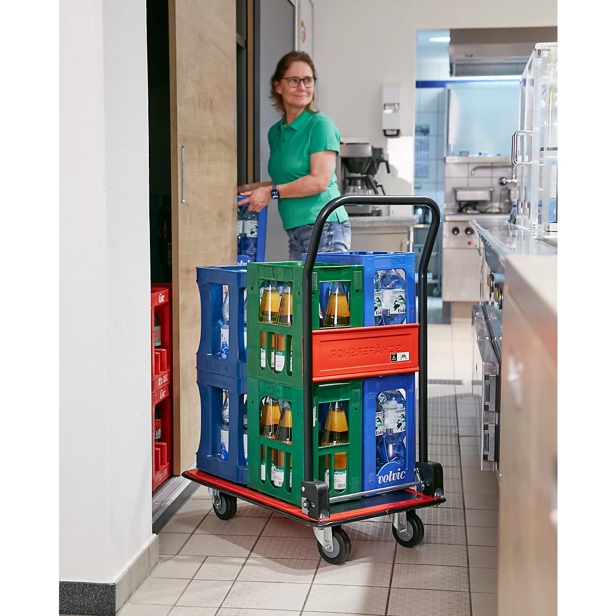 Vrouw met bril duwt een drankwagen met kratten door een gang.