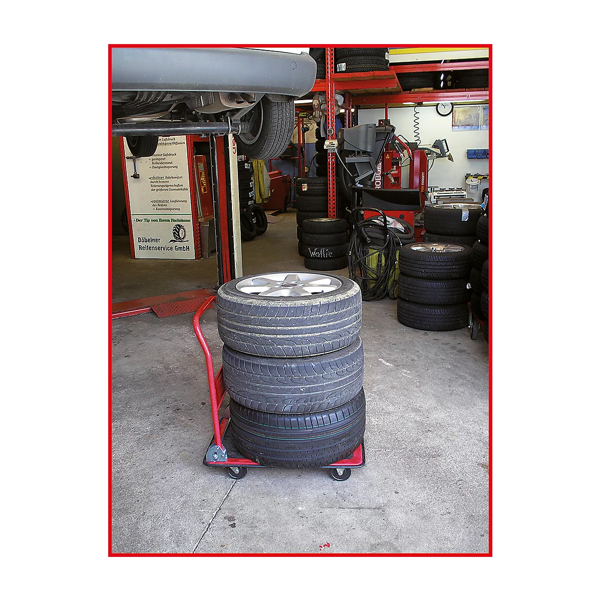 Vier Reifen auf einem roten Wagen in einer Werkstatt; ein Auto wird repariert.