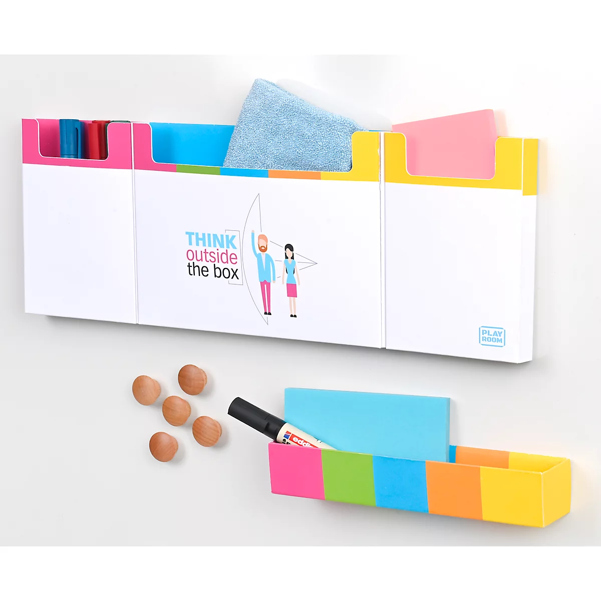 White wall-mounted board with colorful compartments and the words "Think outside the box". Below, another shelf, also with colors. Magnets and pen next to it.
