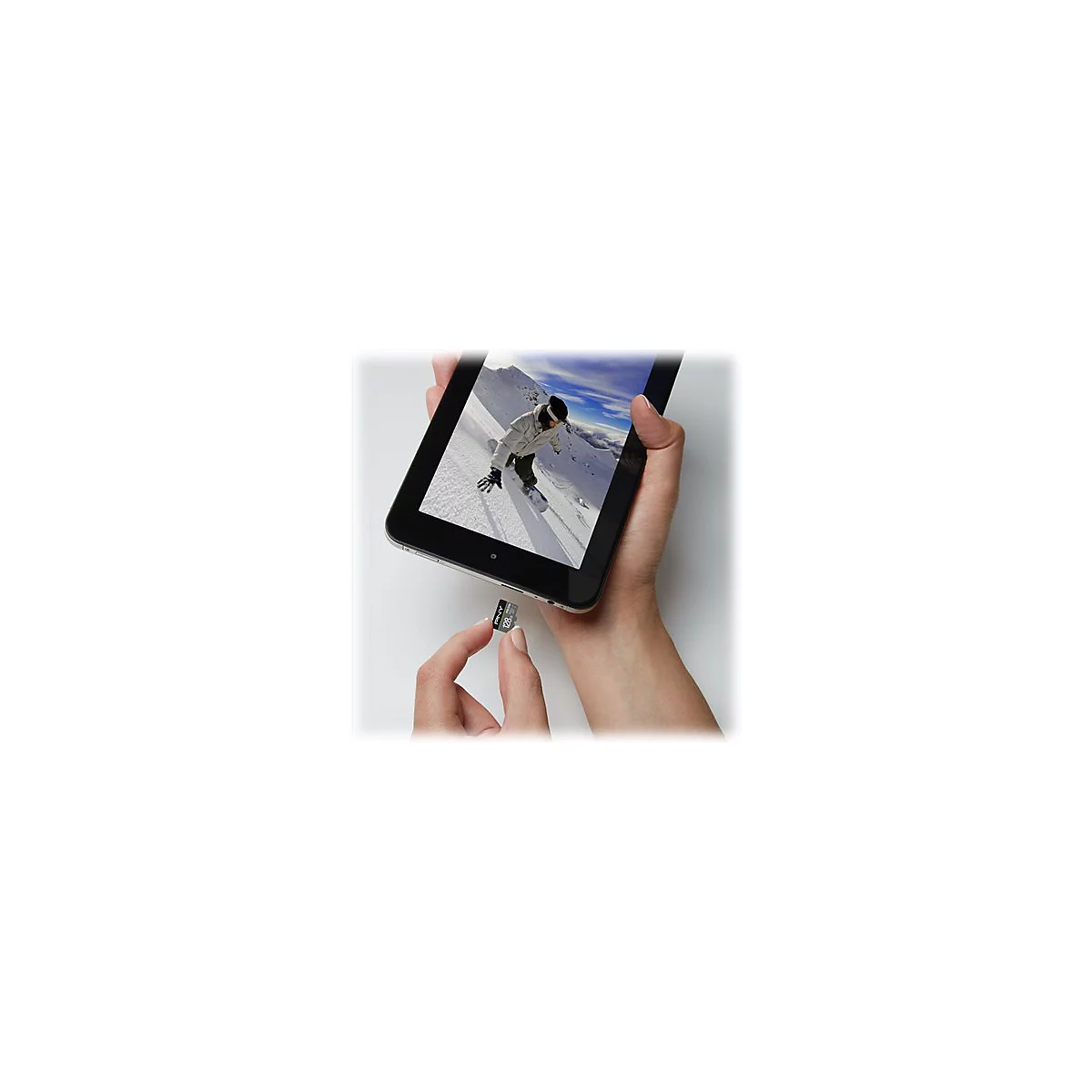 Une main tient une tablette montrant un snowboarder. Une autre main tient une carte SD.