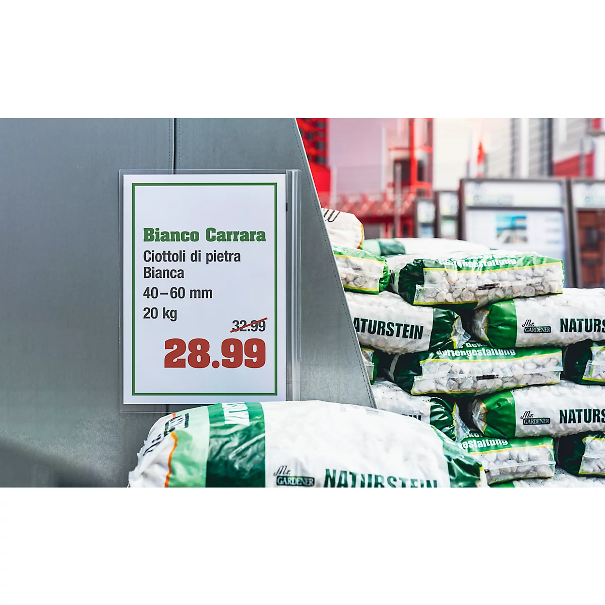 Panneau avec informations sur le produit : "Bianco Carrara" avec prix. Derrière, des piles de pierres dans des emballages plastiques.