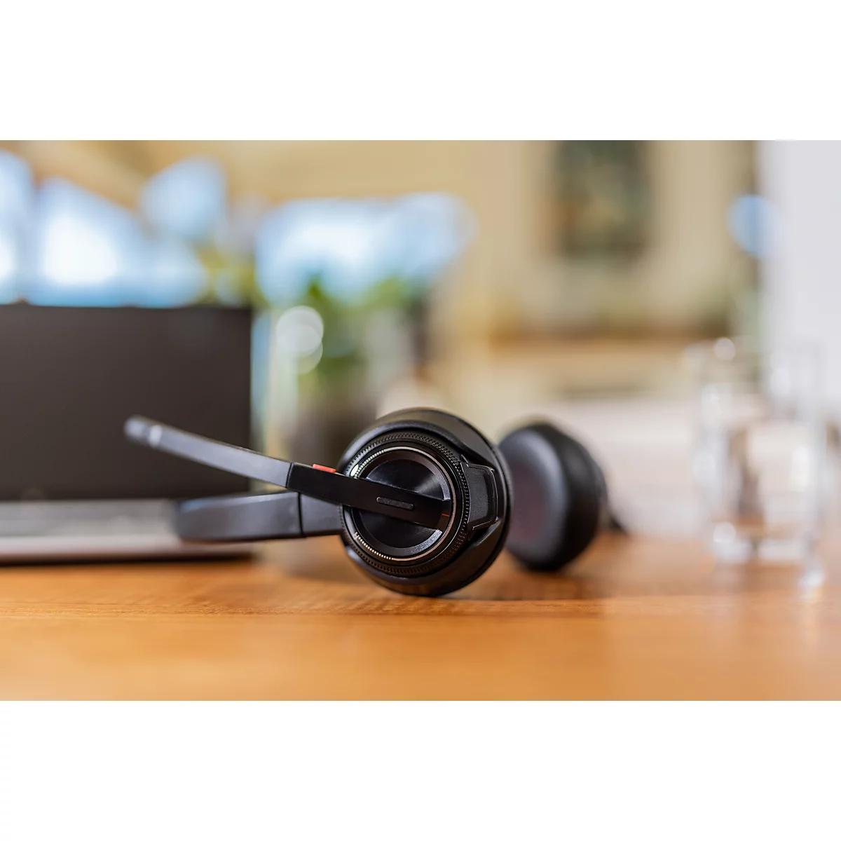 Black headset on wooden surface, laptop and glass in the background.
