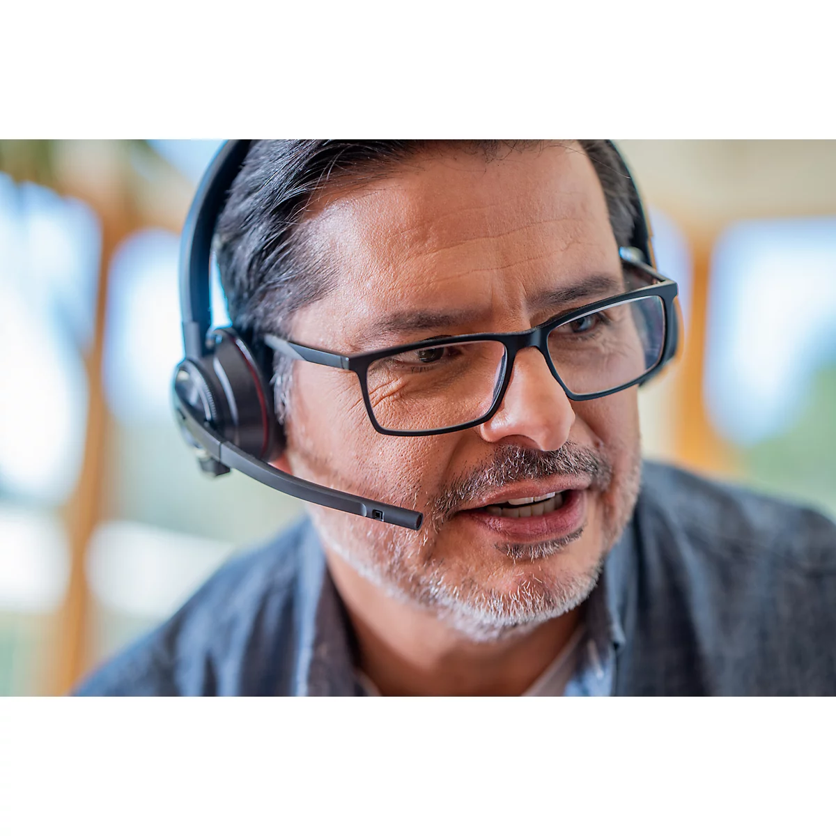 A man wearing glasses and a headset is speaking. He is looking slightly to the side.