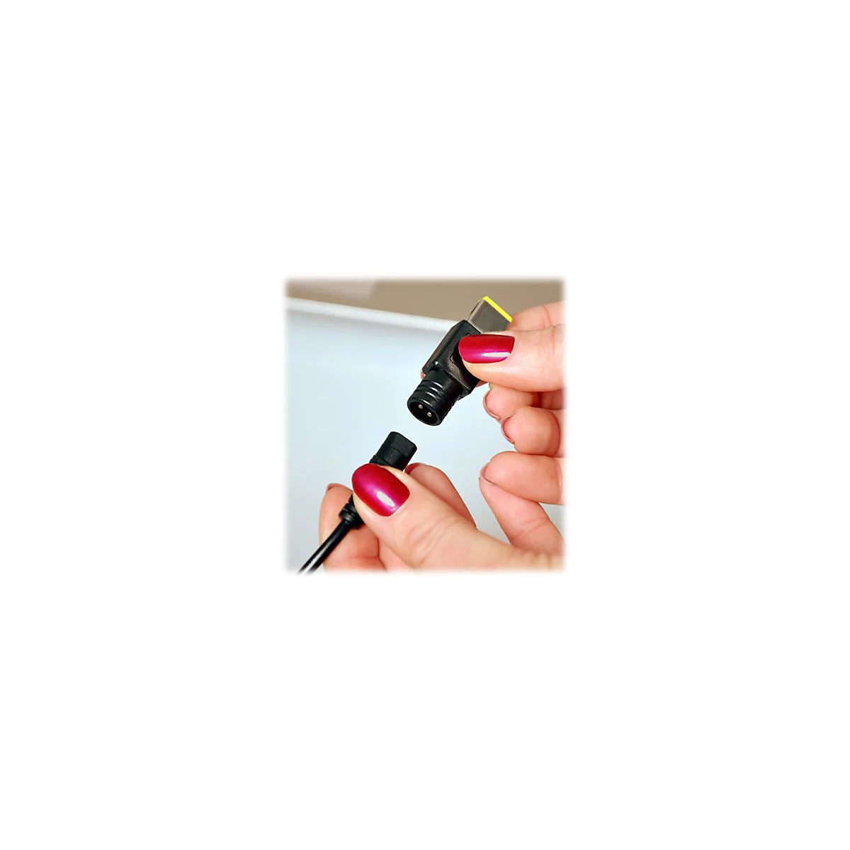 HÃ¤nde halten einen schwarzen Stecker und einen Stecker, die verbunden werden. Die Finger haben roten Nagellack.