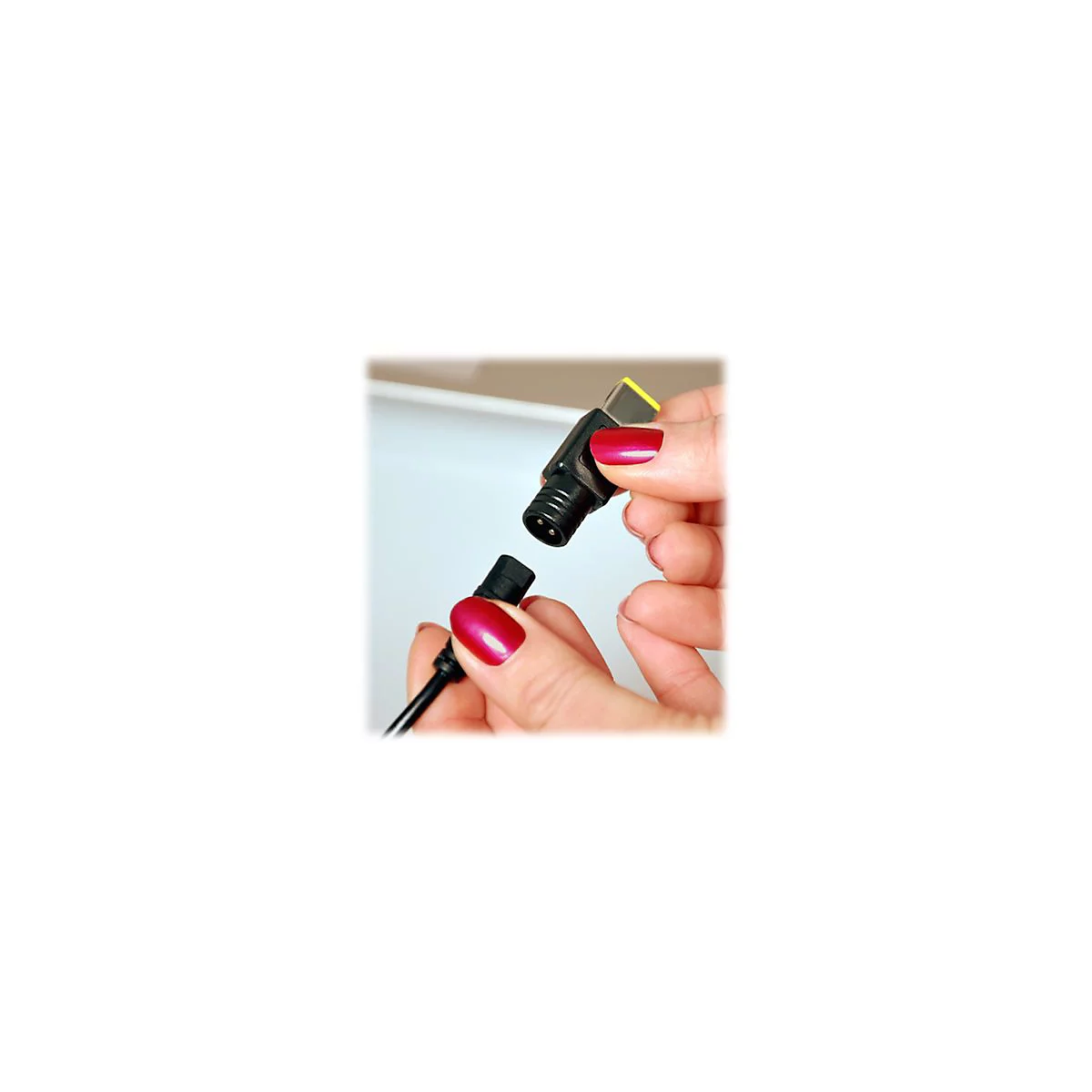 Gros plan sur deux mains connectant un connecteur d'alimentation noir. Vernis Ã  ongles rouge, fond blanc.