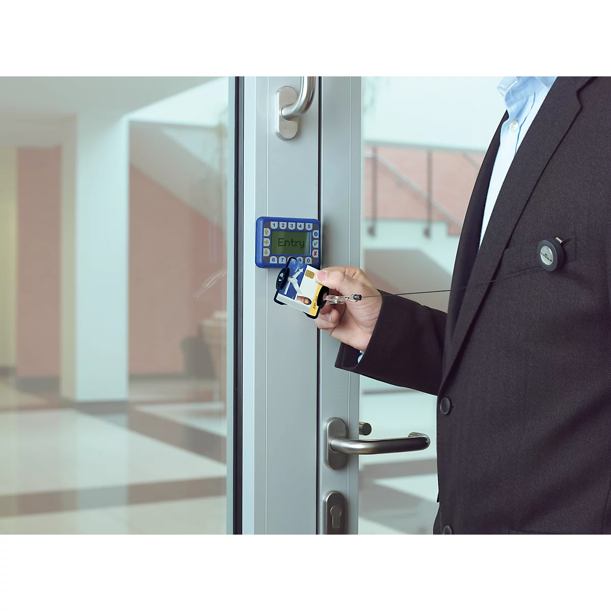Une personne en costume ouvre une porte vitrée avec un lecteur de cartes.