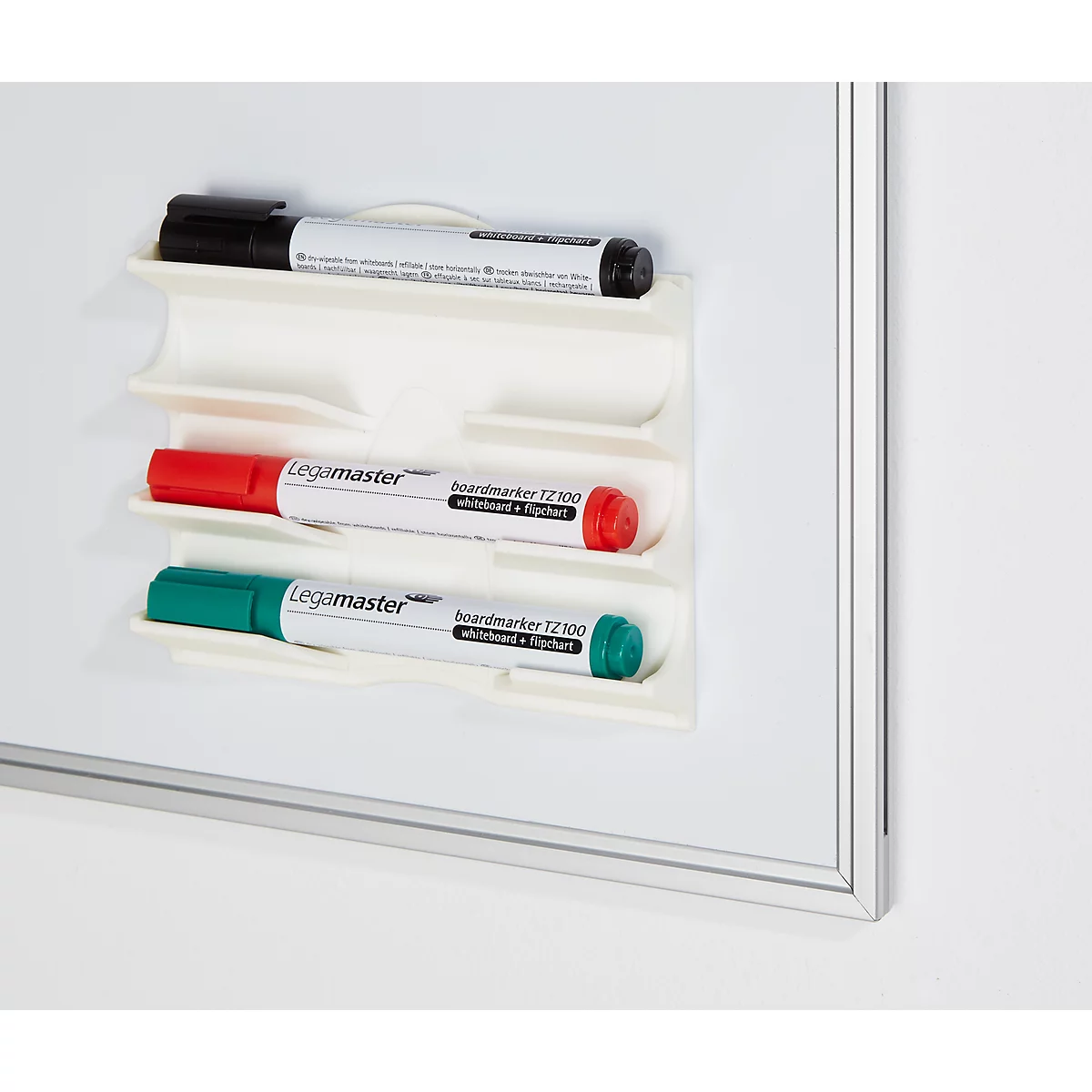 Trois marqueurs pour tableau blanc dans un support, sur un tableau blanc. Noir en haut, rouge au milieu, vert en bas.