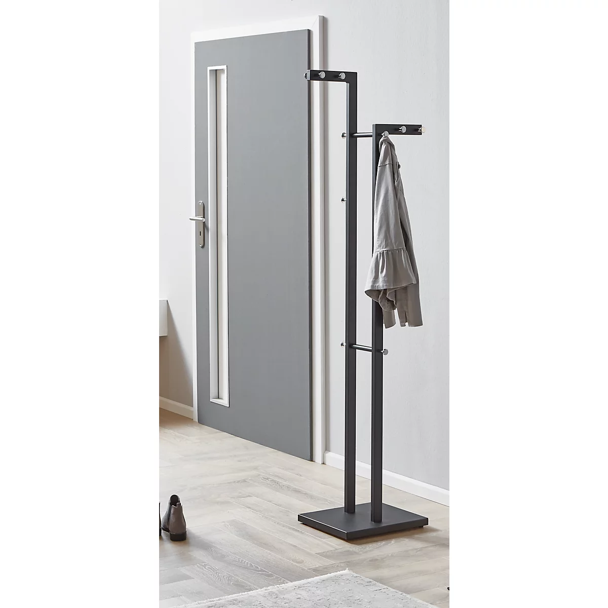 Portemanteau gris, autoportant, avec veste. Derrière le porte-manteau, une porte grise.