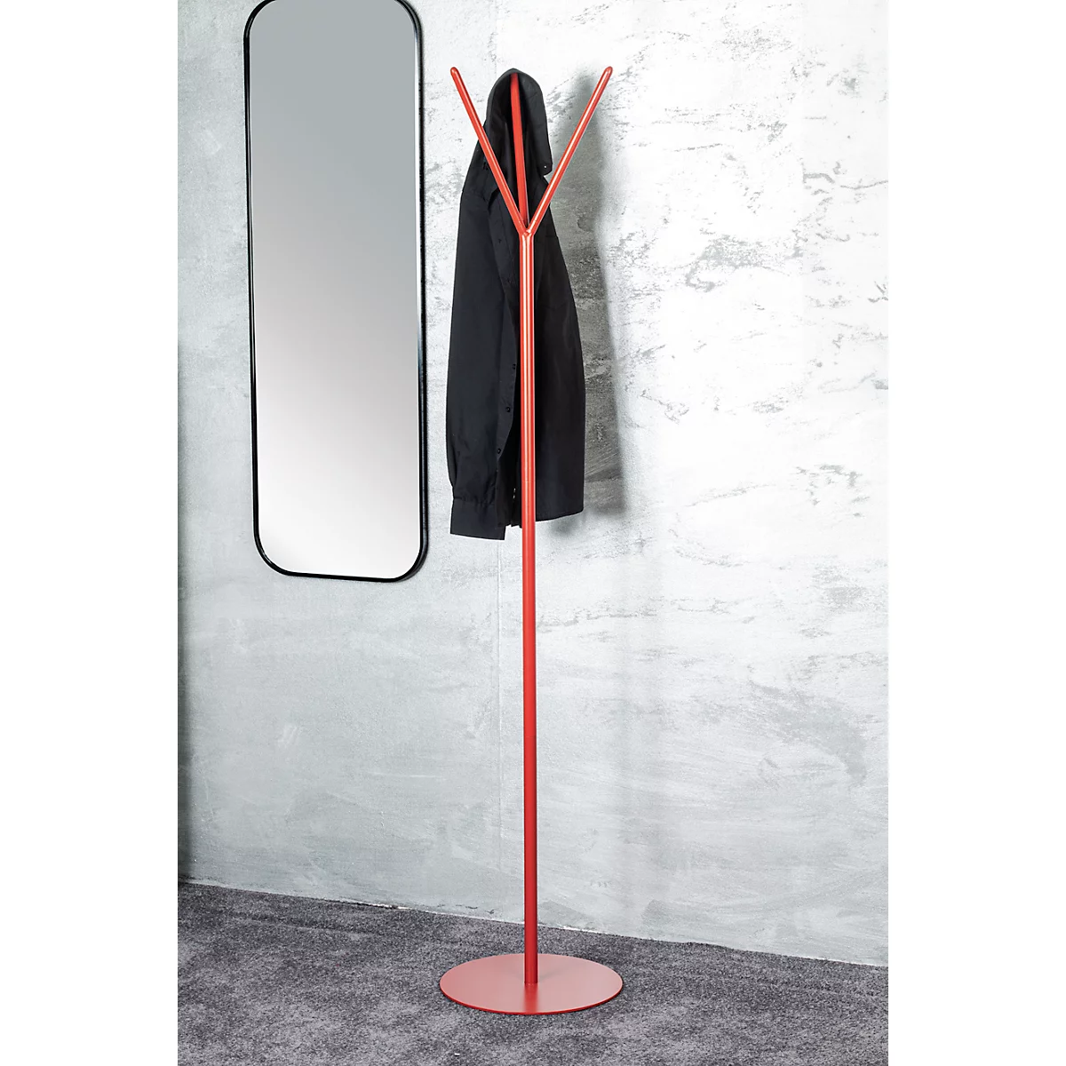 Porte-manteau rouge avec manteau noir, à côté d'un miroir noir sur un mur gris.