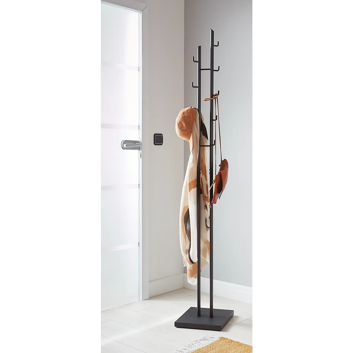 Porte-manteau noir avec chapeau, écharpe et sac. Il se trouve dans un couloir devant une porte blanche.
