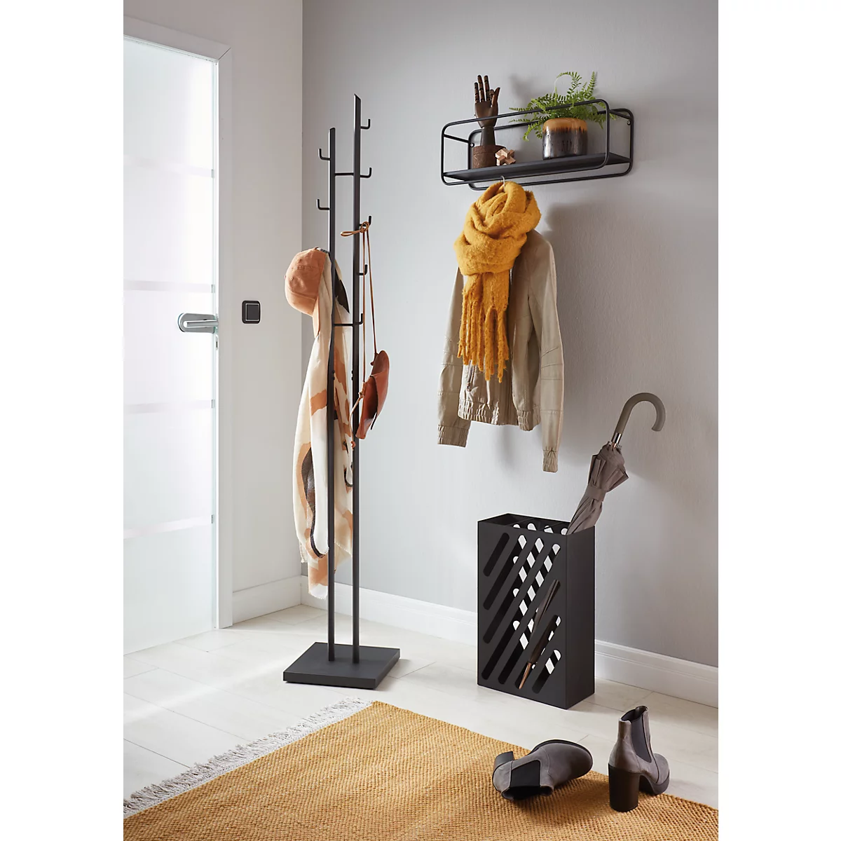 Porte-manteau noir avec manteaux, écharpe, chapeau et gants. Sur une étagère : décoration, plante. Parapluie, bottes et tapis au sol.
