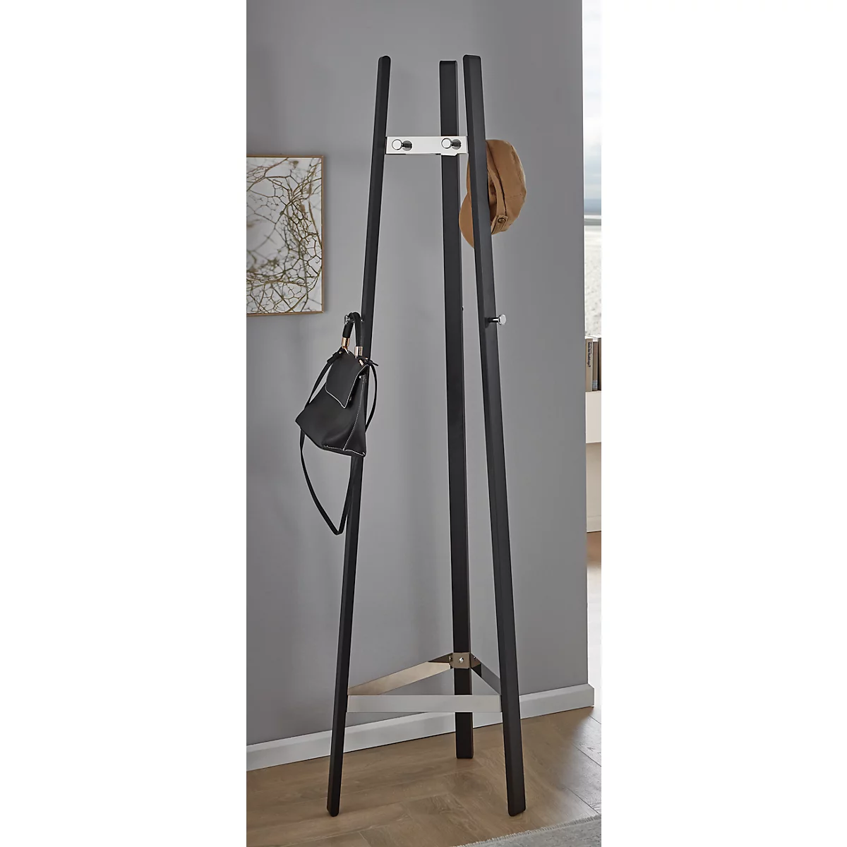 Porte-manteau noir avec chapeau et sac à main. Sur parquet clair contre un mur gris.