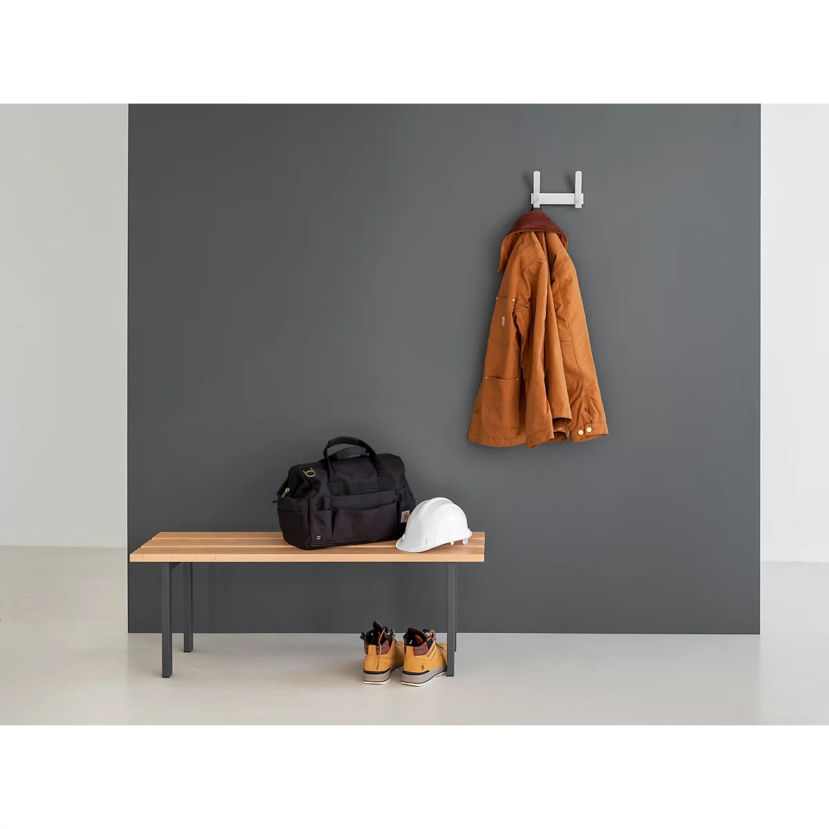 Porte-manteau mural avec veste marron, sac noir, casque et chaussures. Un crochet mural est sous la veste.