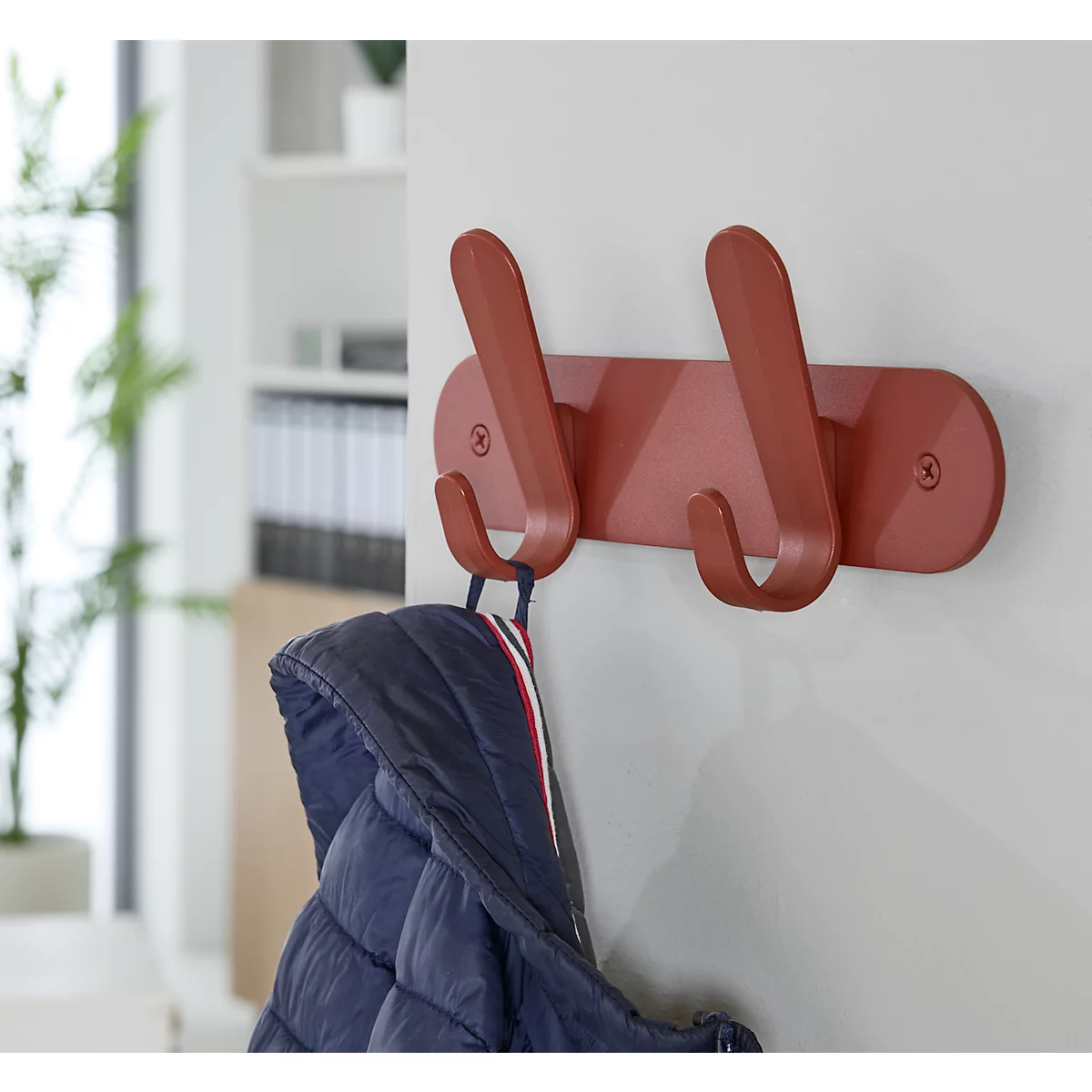 Patère murale rouge avec deux crochets, avec une veste bleue accrochée.