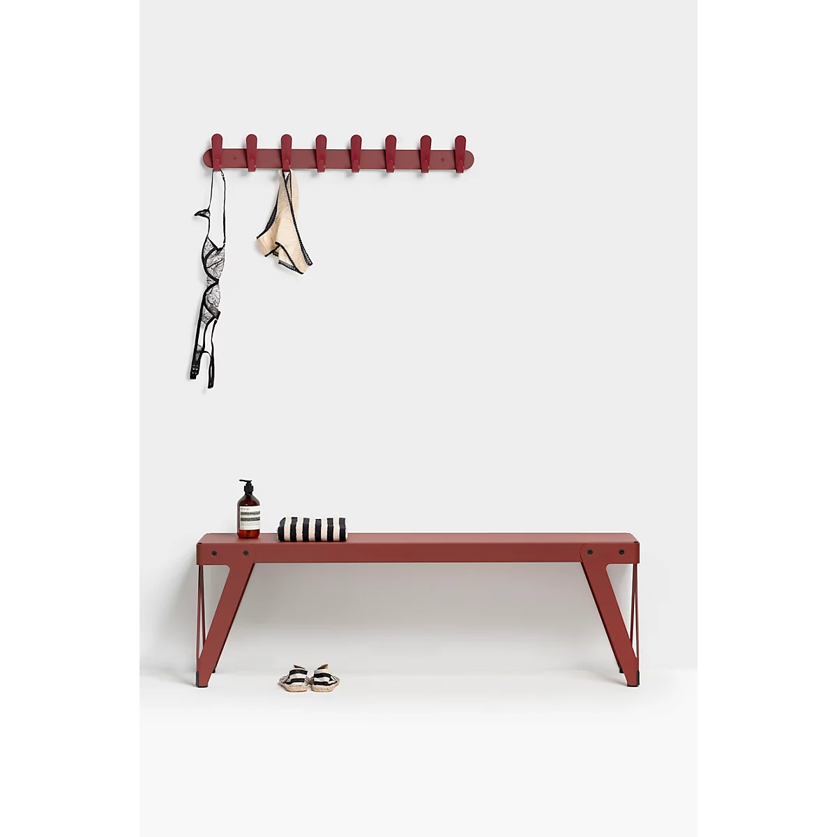 Banc rouge avec porte-manteau. Soutien-gorge et sous-vêtements y sont accrochés. Sur le banc, une bouteille, une serviette et des chaussures.