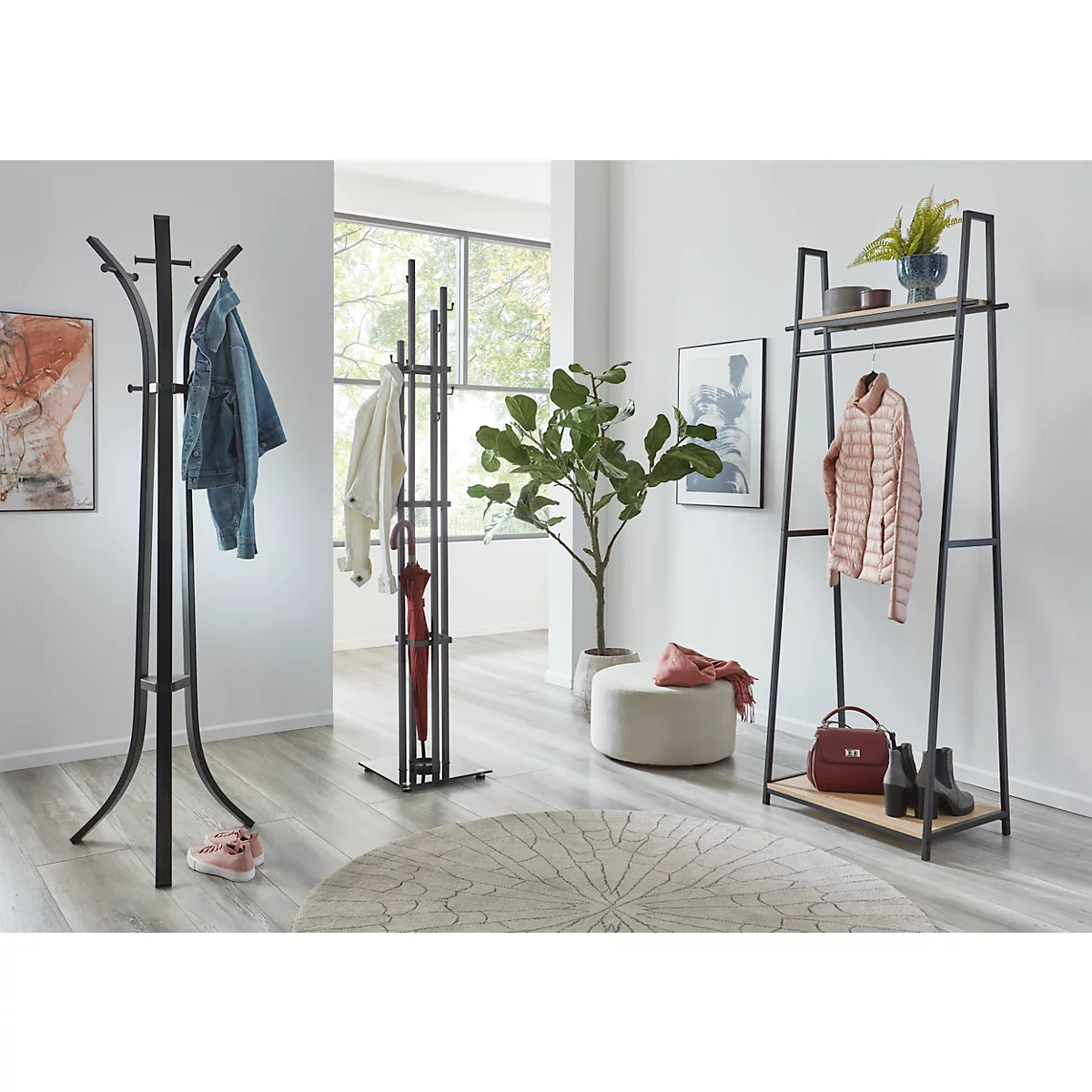 Un couloir lumineux avec des portemanteaux, des vêtements, une plante et un tapis rond.