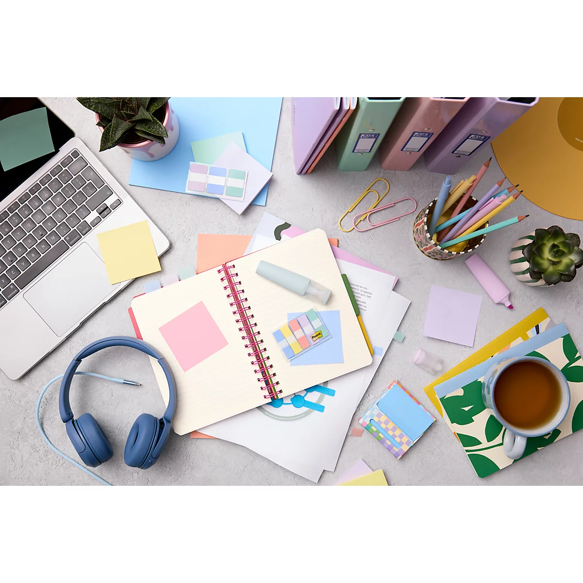 Vue de dessus d'un bureau avec un ordinateur portable, un carnet, un casque, des stylos et une tasse de thé.