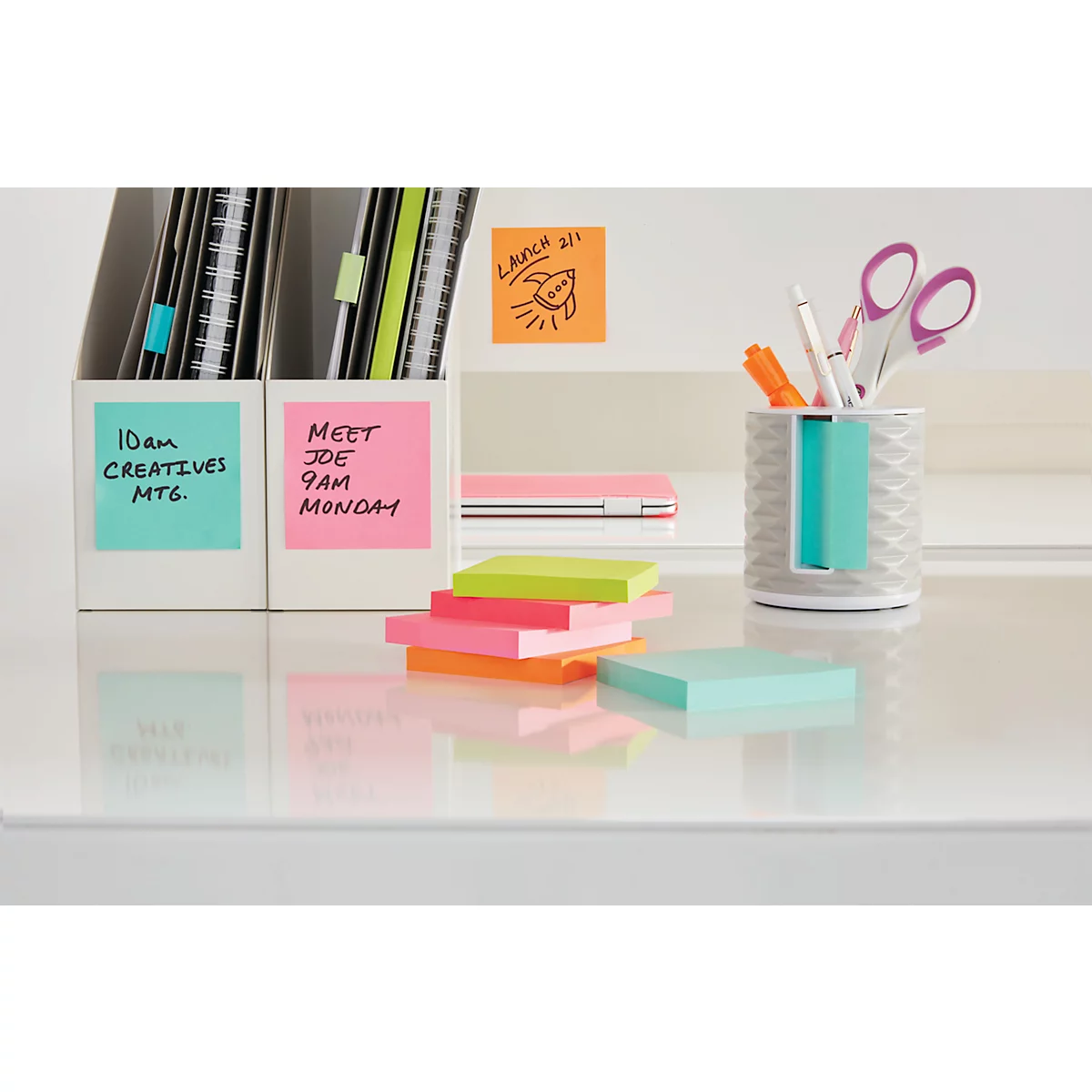 Gros plan d'un bureau avec des post-it. Texte sur des post-it roses, verts et orange. Une fusée est représentée sur un post-it orange.