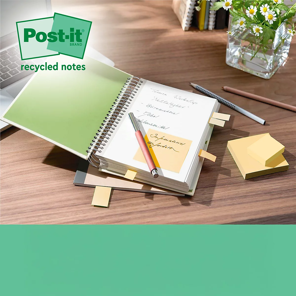 Ein offenes Notizbuch mit Post-it-Zetteln, Stift und Blumen auf einem Holztisch. Im Hintergrund ein Laptop.