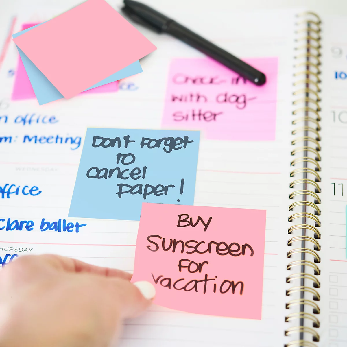 Gros plan d'un agenda avec des post-it. Sur un post-it rose, on peut lire : "Acheter de la crème solaire pour les vacances."
