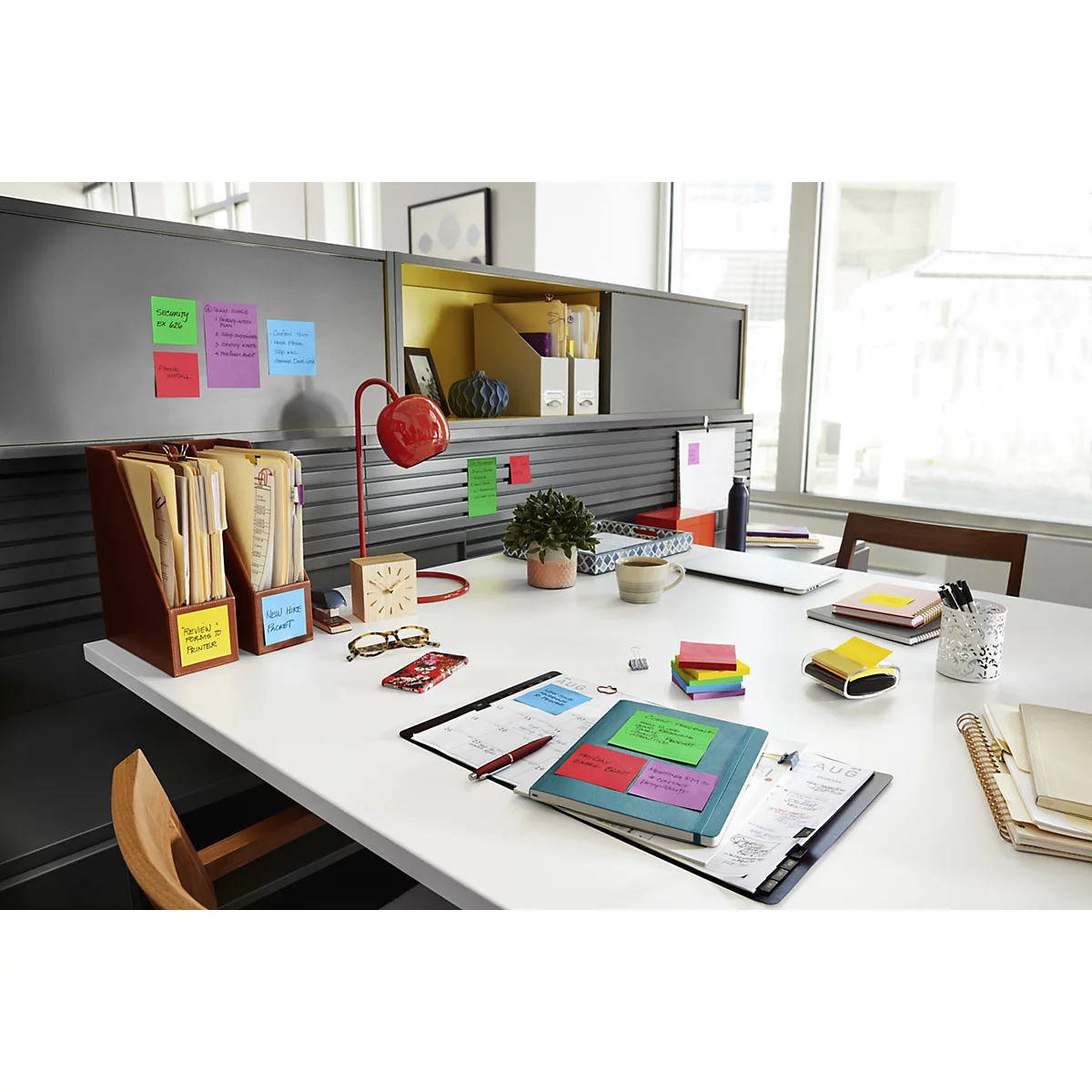A desk with colorful sticky notes, folders, a lamp, and other office supplies. Focus on the sticky notes.