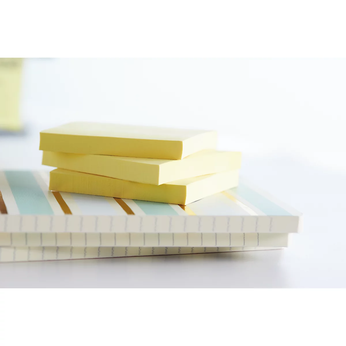 Des post-it jaunes reposent sur un bloc-notes à rayures. L'image montre un gros plan de fournitures de bureau sur fond blanc.