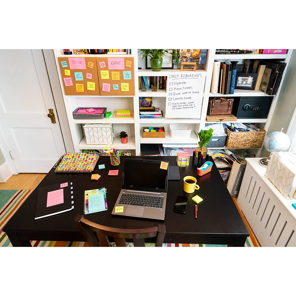 Schreibtisch mit Laptop, Notizen, Kaffee, Büchern und Post-its. Im Hintergrund ein Regal mit Notizen und Büchern.