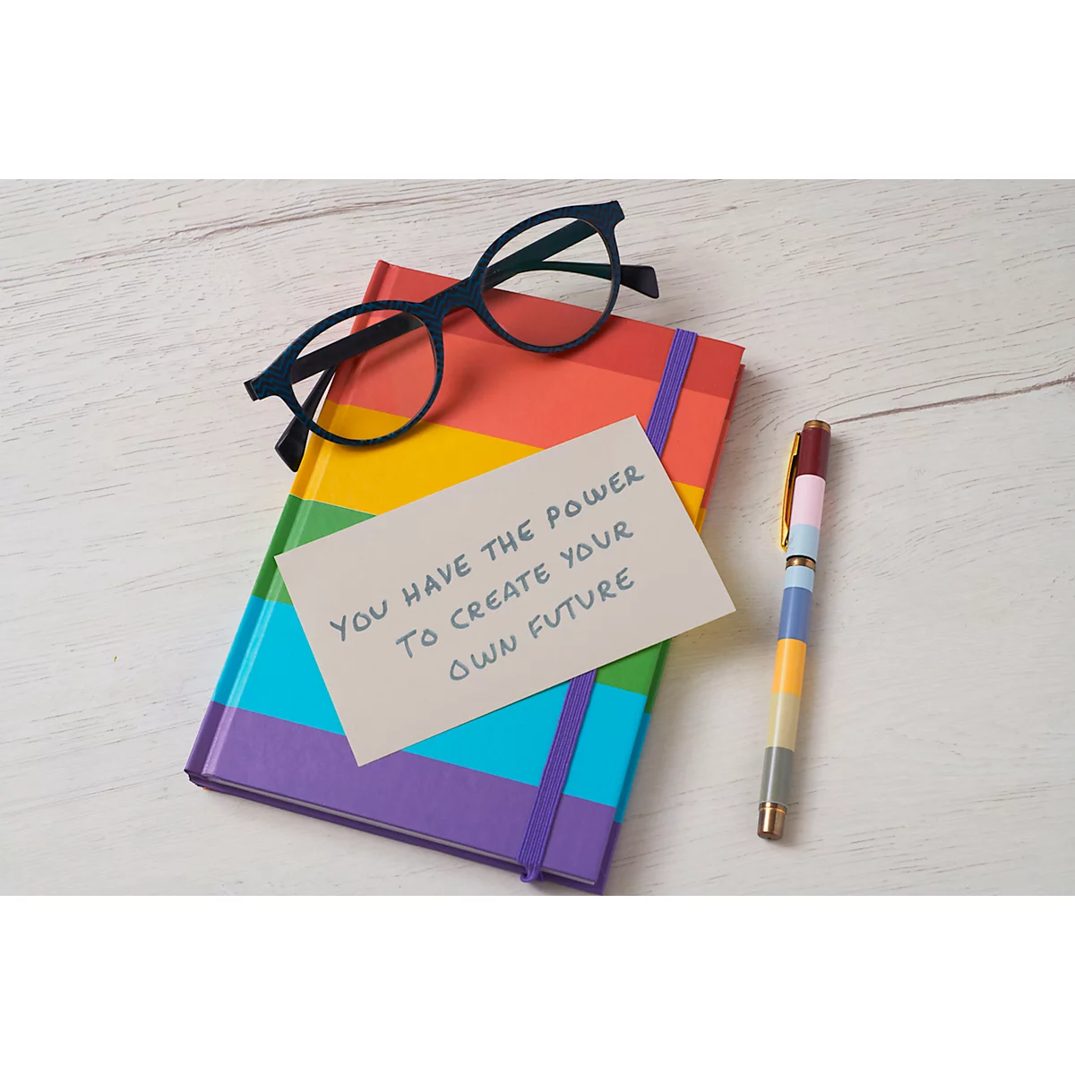 Carnet aux couleurs de l'arc-en-ciel, lunettes, stylo et carte avec le texte: "You have the power to create your own future".