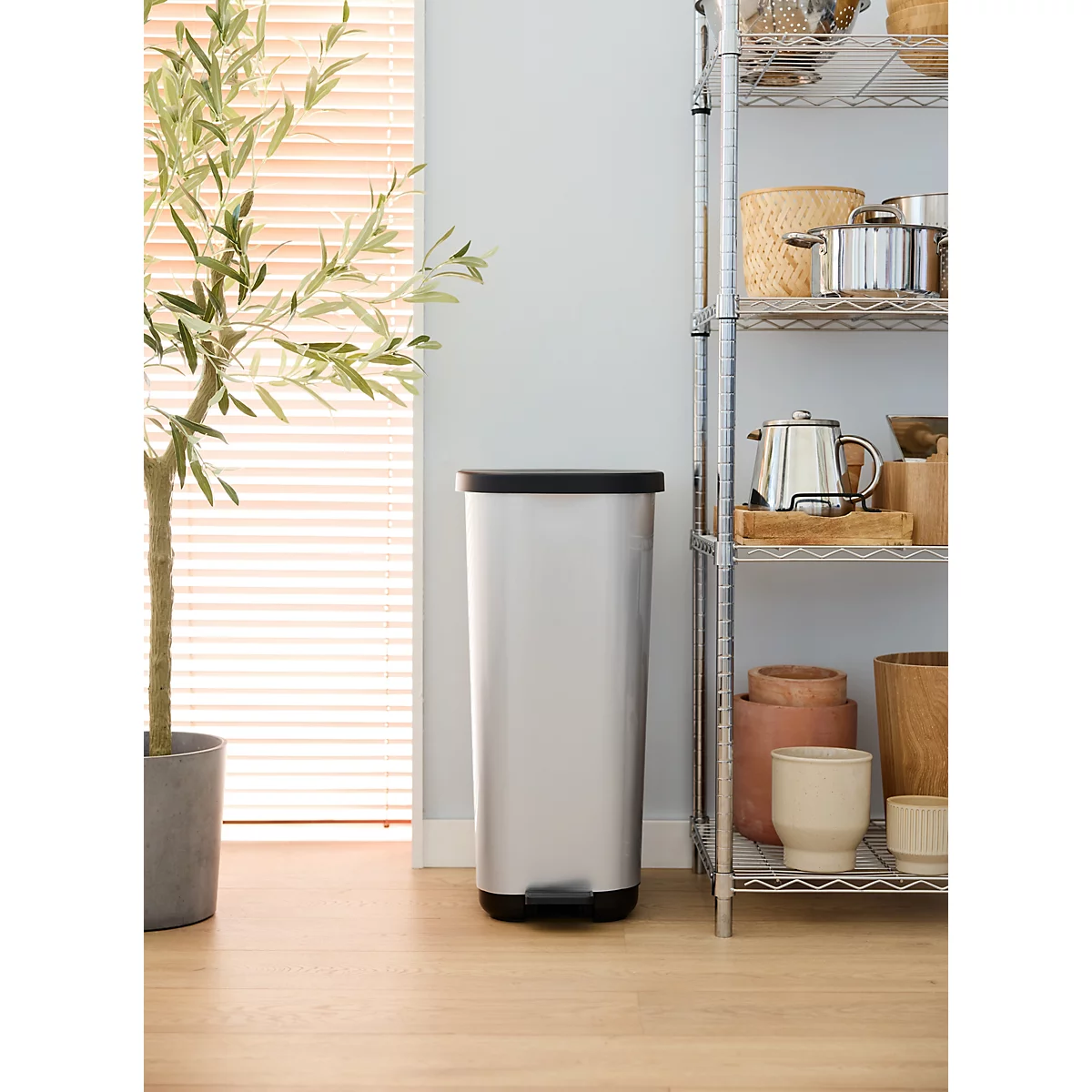 Une poubelle argentée avec le couvercle ouvert et un sac poubelle jaune à l'intérieur. À côté, une personne avec des chaussures marron.