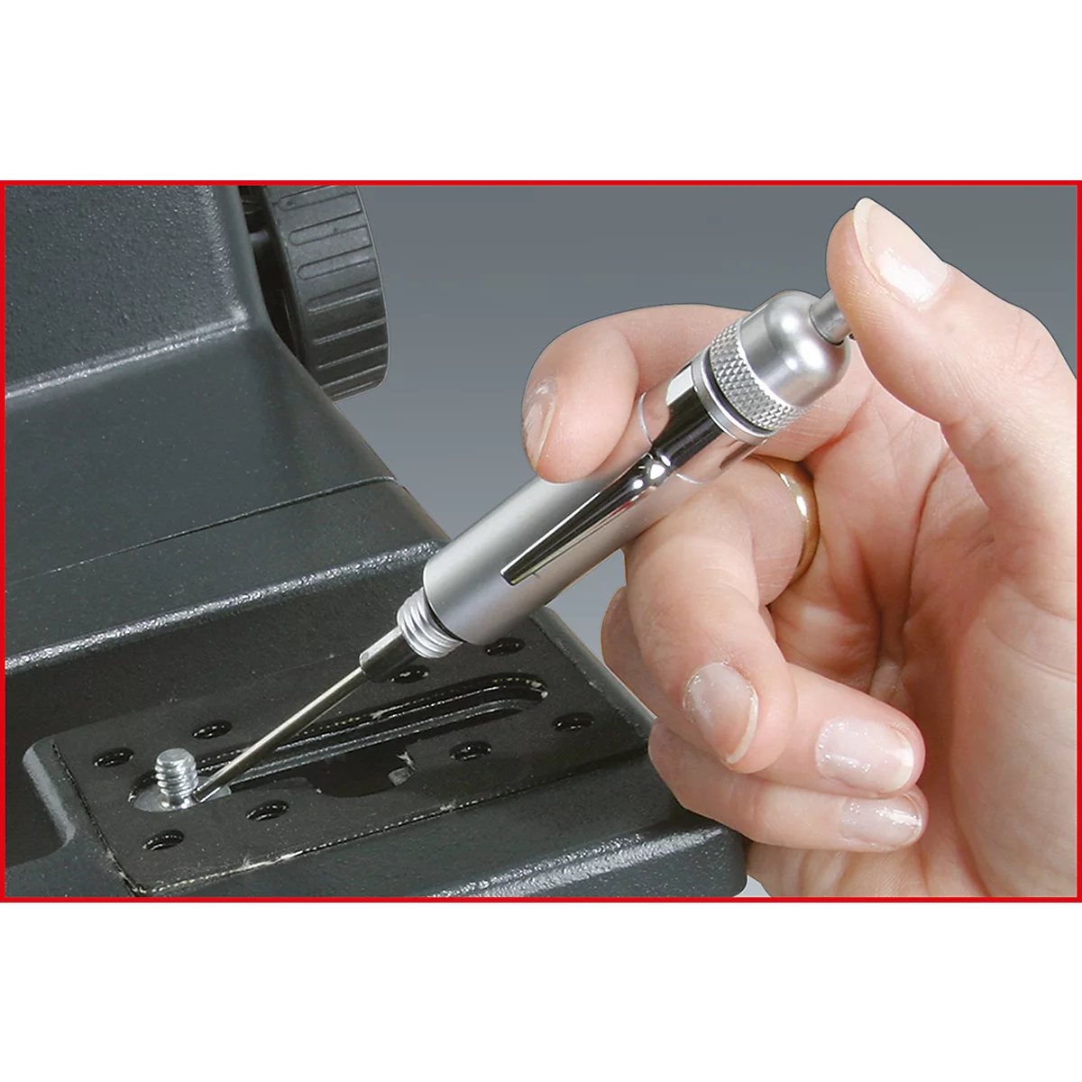 Eine Hand hält einen silberfarbenen Schraubendreher. Dieser wird gerade in eine Schraube an einer schwarzen Kamerahalterung eingeführt.