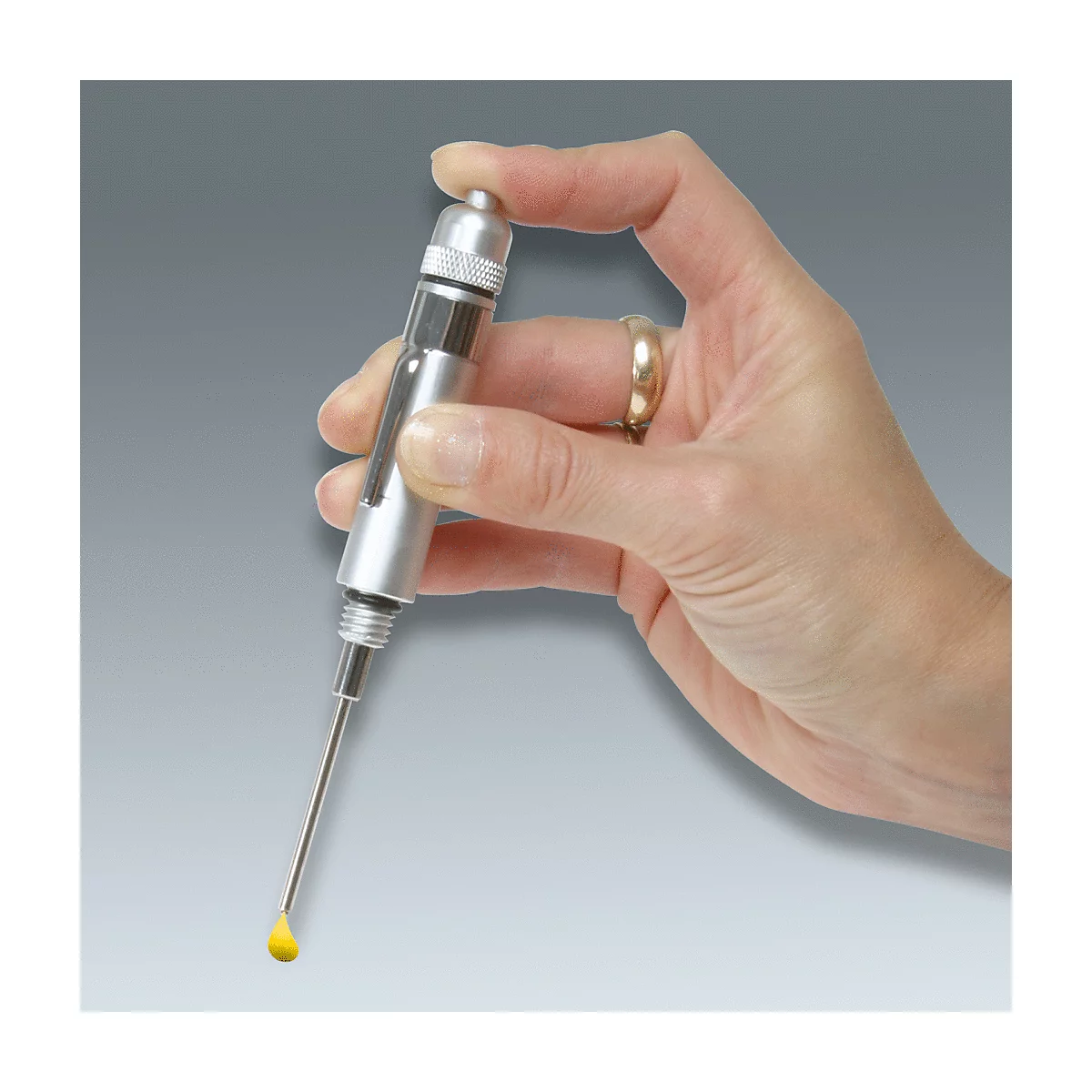Hand hält eine Spritze. Am Ende der Nadel tropft eine gelbe Flüssigkeit.