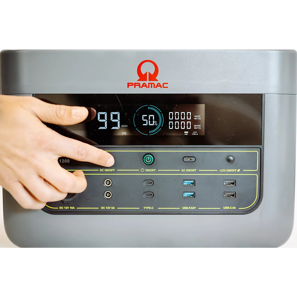 Hand drückt einen Knopf auf dem Bedienfeld einer grauen Pramac Powerstation mit digitaler Ladeanzeige.