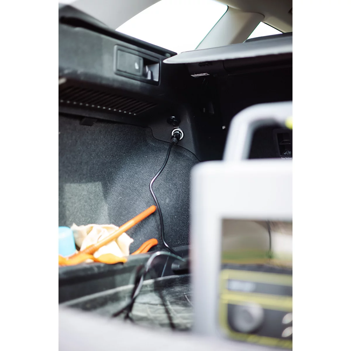 Ein im Kofferraum eines Autos angeschlossenes Ladegerät mit schwarzem Kabel an der 12-Volt-Steckdose.