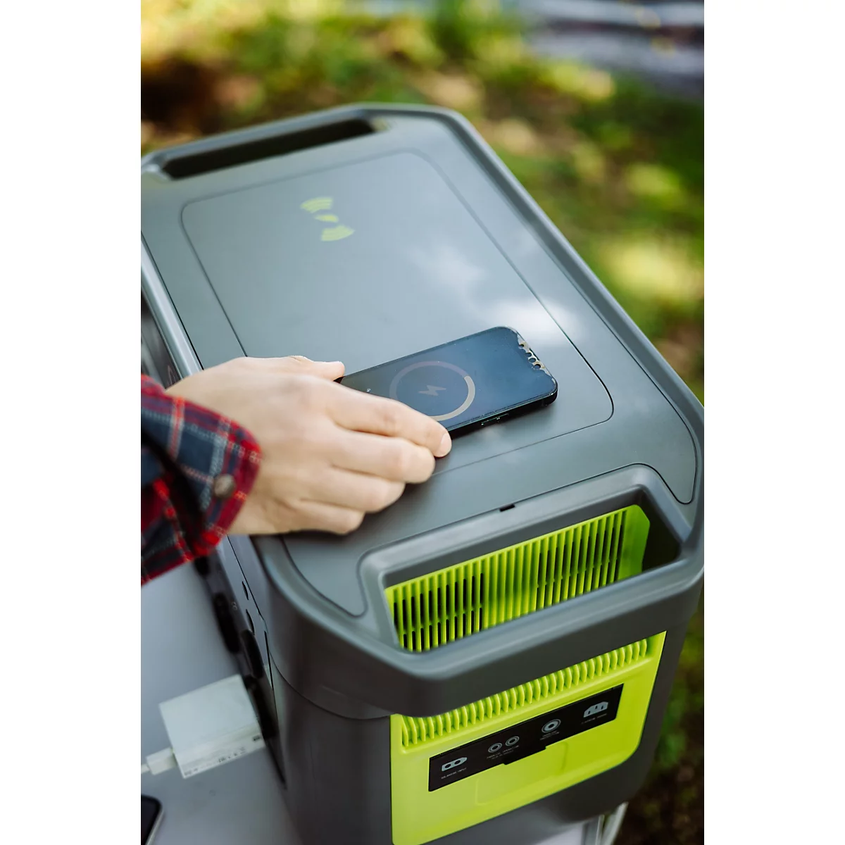 Eine Hand legt ein Smartphone zum kabellosen Laden auf eine graue Powerstation mit neongrünen Akzenten.