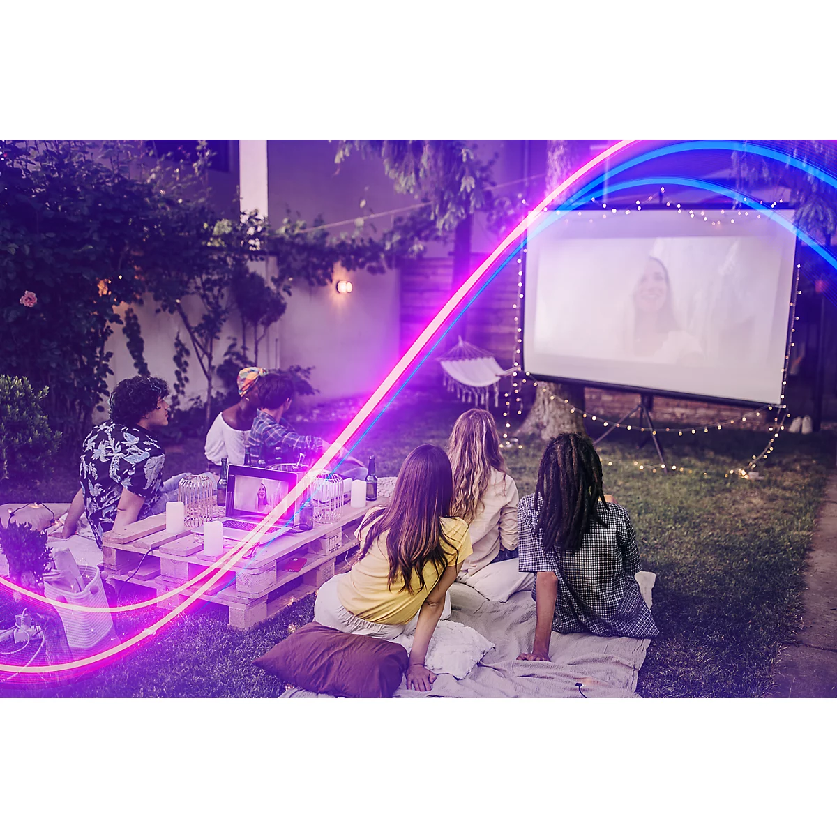 Gruppe von Freunden schaut abends im Garten einen Film auf einer Leinwand, mit Lichterketten und Neon-Effekten.