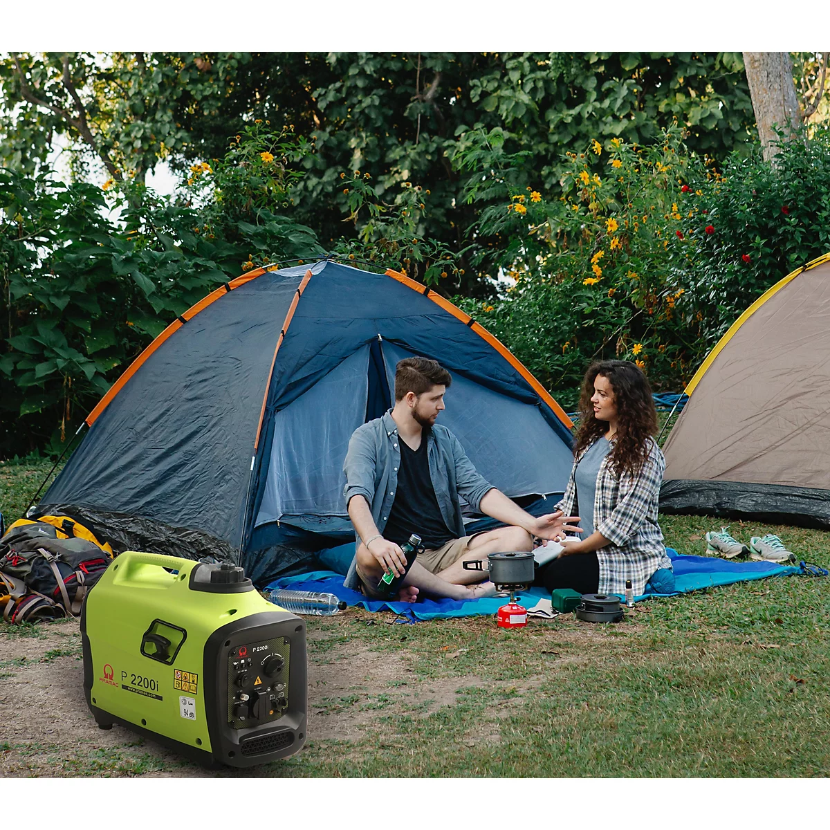 Ein Paar beim Camping vor einem Zelt mit einem grünen Stromerzeuger im Vordergrund.