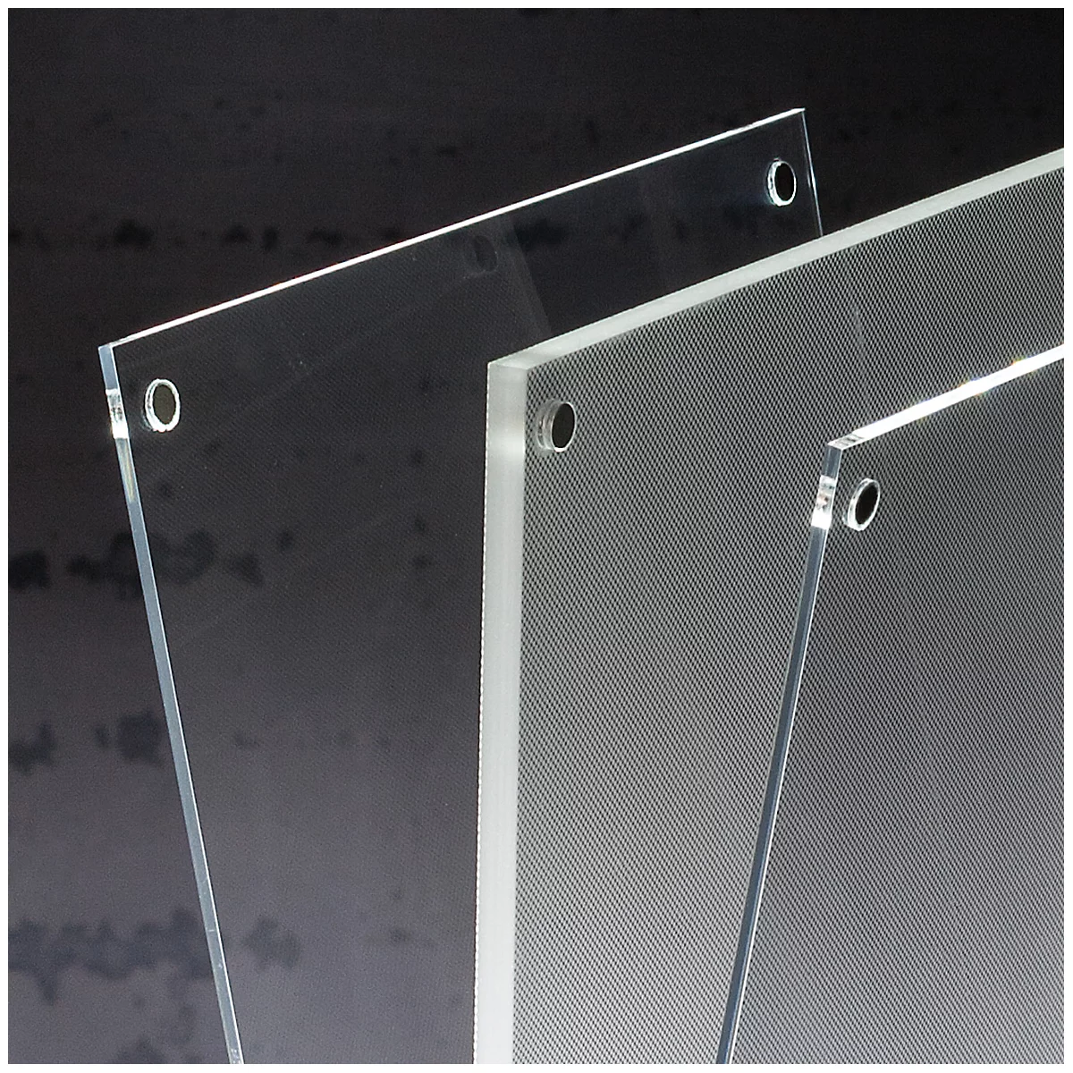 Close-up of three transparent acrylic plates with holes. The plates are partially corrugated and placed against a dark background.