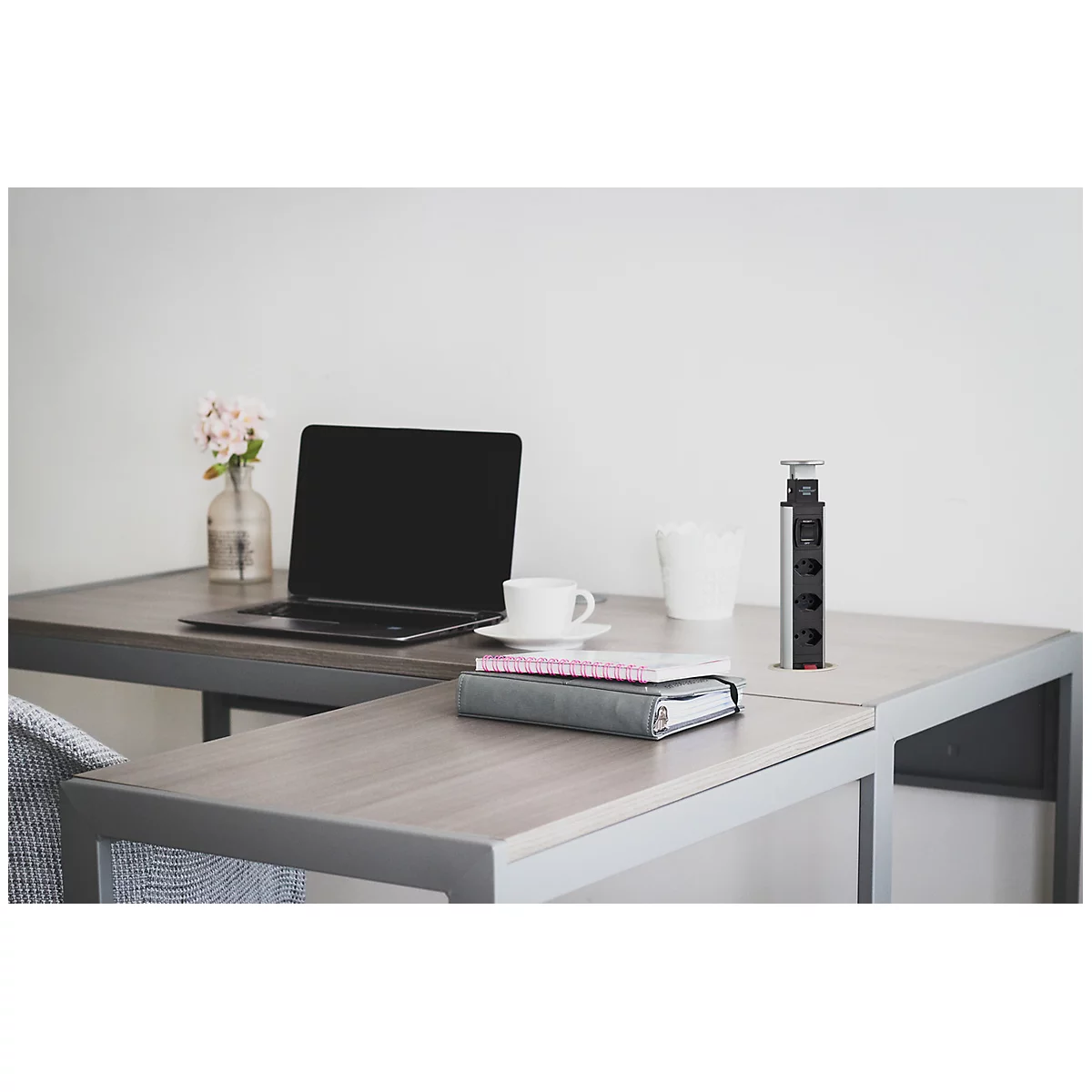 Un bureau moderne avec un ordinateur portable, une tasse de café, un vase de fleurs et une multiprise.
