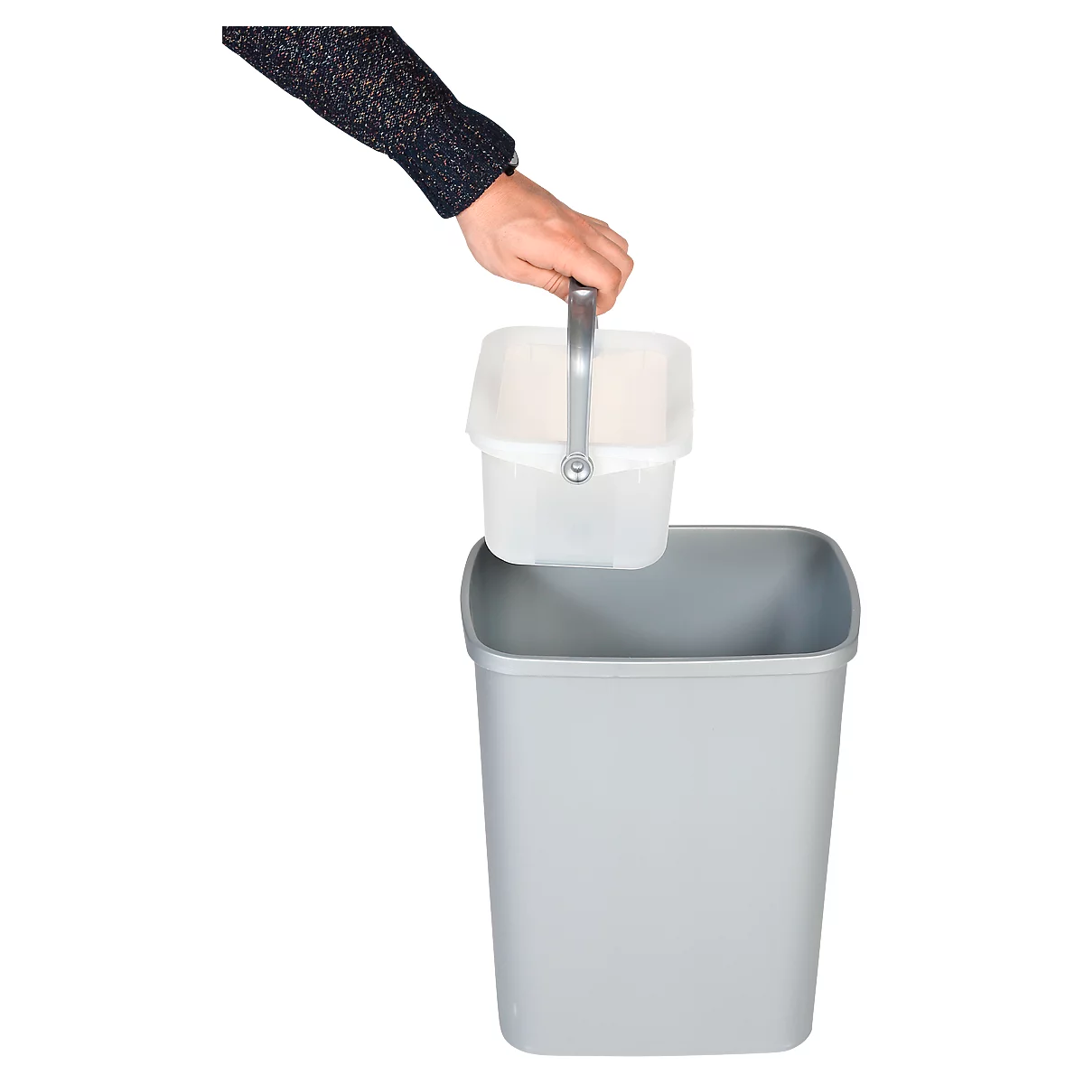Een hand tilt een kleine, witte emmer met een handvat uit een grijze vuilnisbak. De achtergrond is wit.