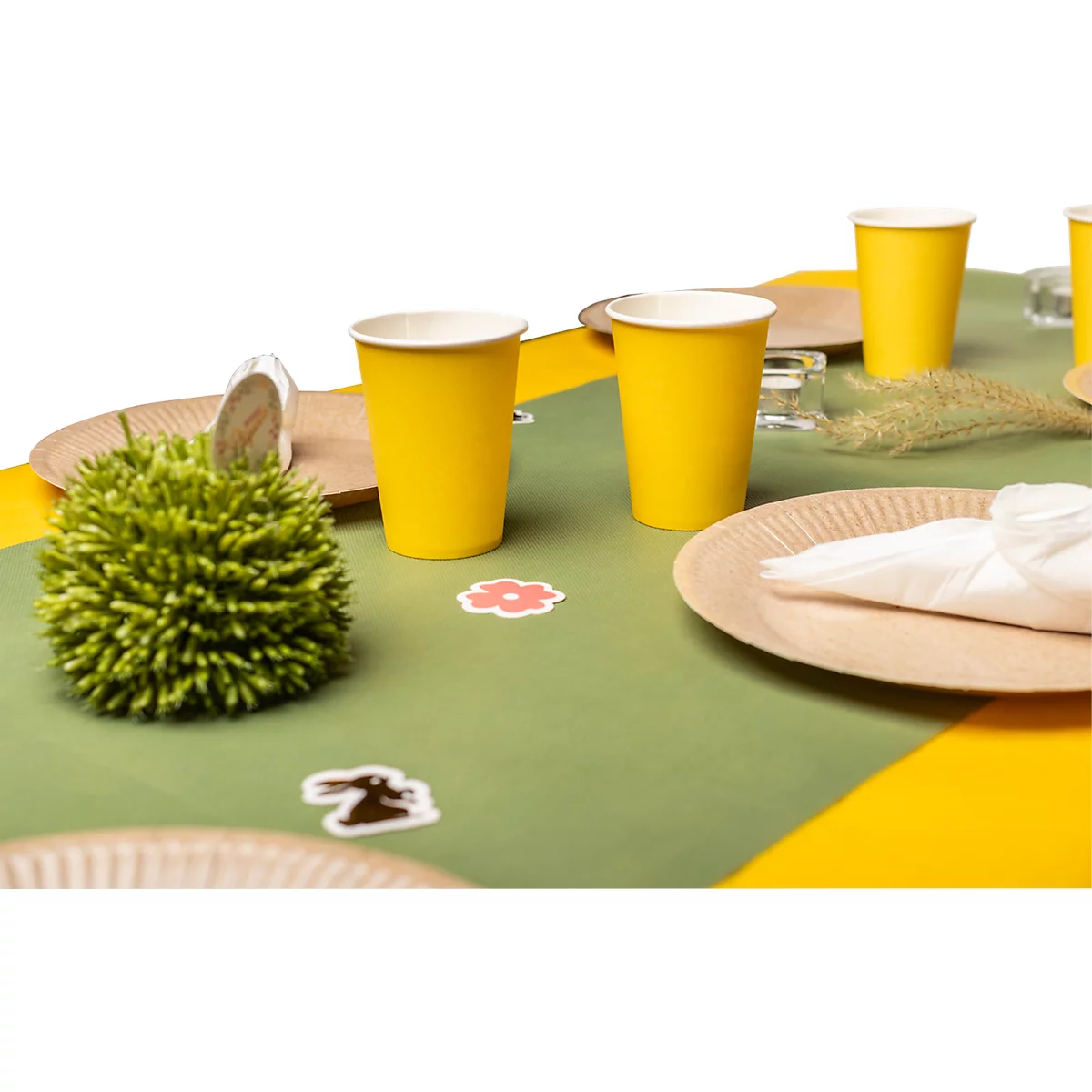Gros plan d'une table de Pâques. Gobelets jaunes, assiettes en carton et nappe verte avec éléments décoratifs.