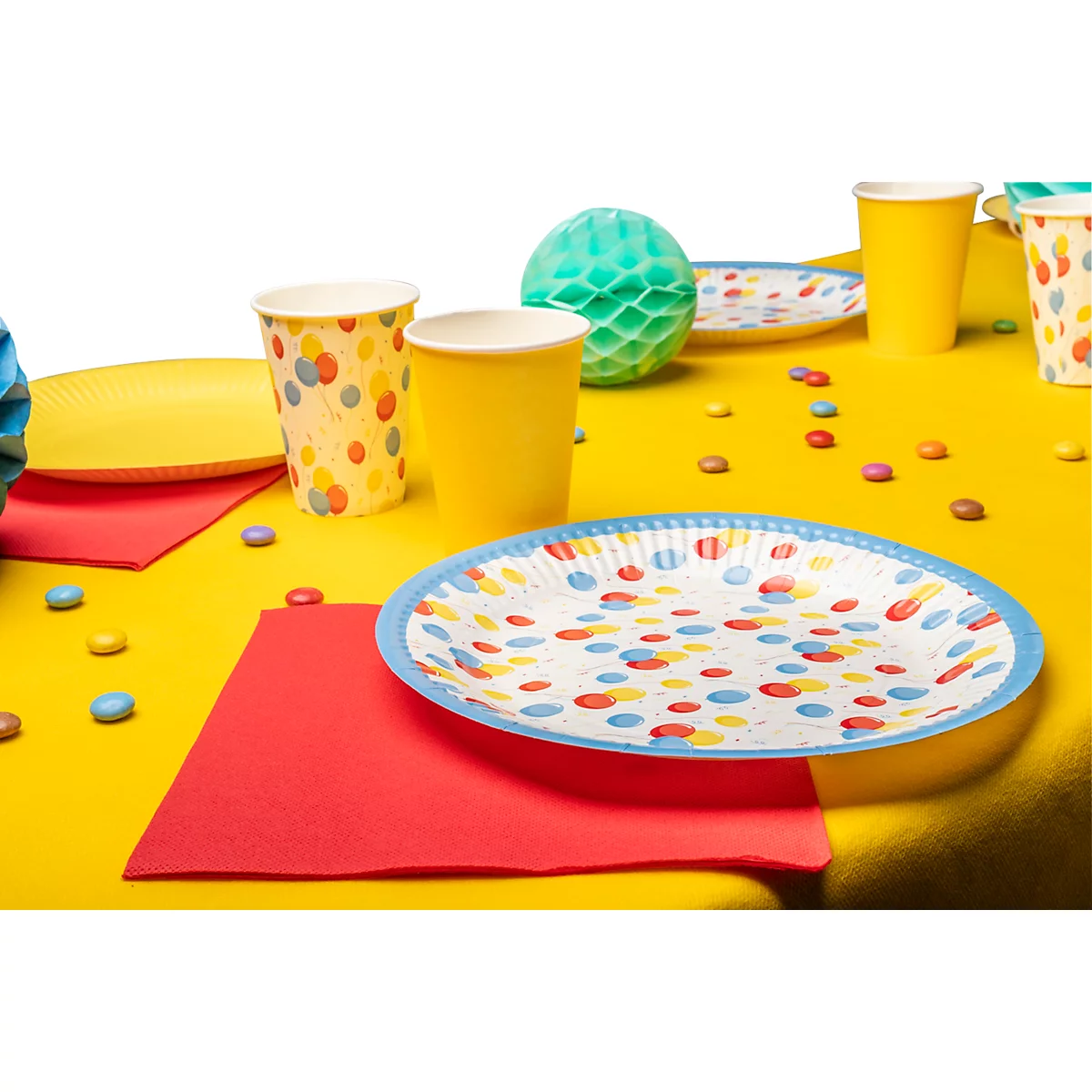 Table jaune avec décorations de fête : assiettes, gobelets, serviettes, bonbons et ballons.