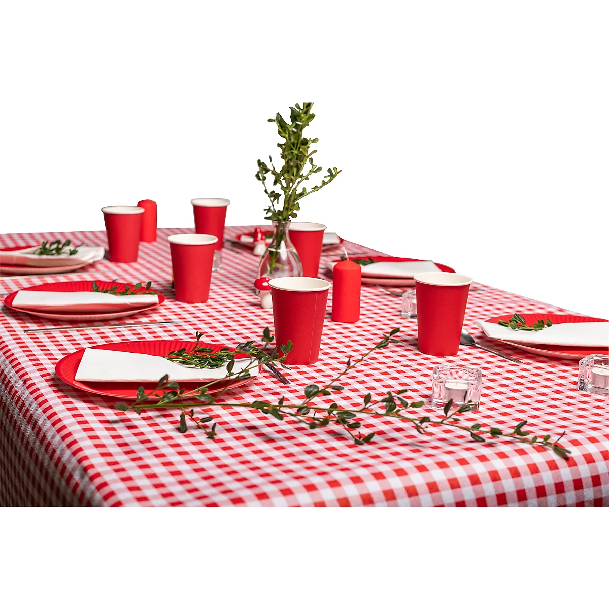 Une table est dressée avec une nappe à carreaux rouges. Des assiettes, des gobelets, des bougies et des branches vertes sont sur la table.