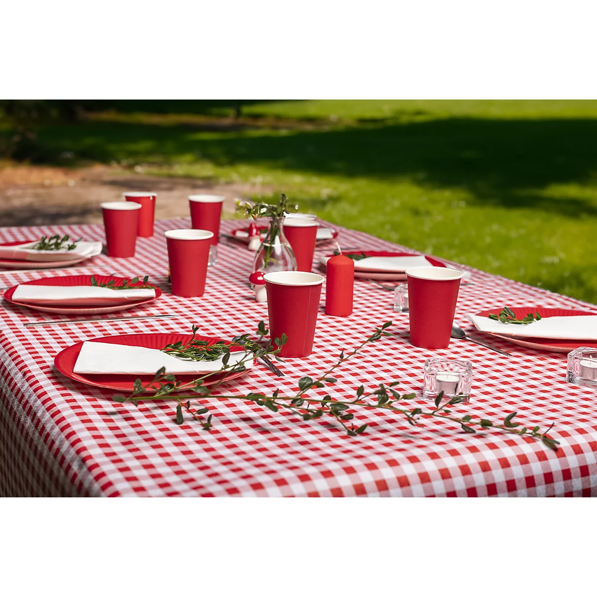 Une table de pique-nique avec une nappe à carreaux rouge et blanc. Des gobelets en papier rouges, des assiettes et un vase de fleurs sont sur la table.