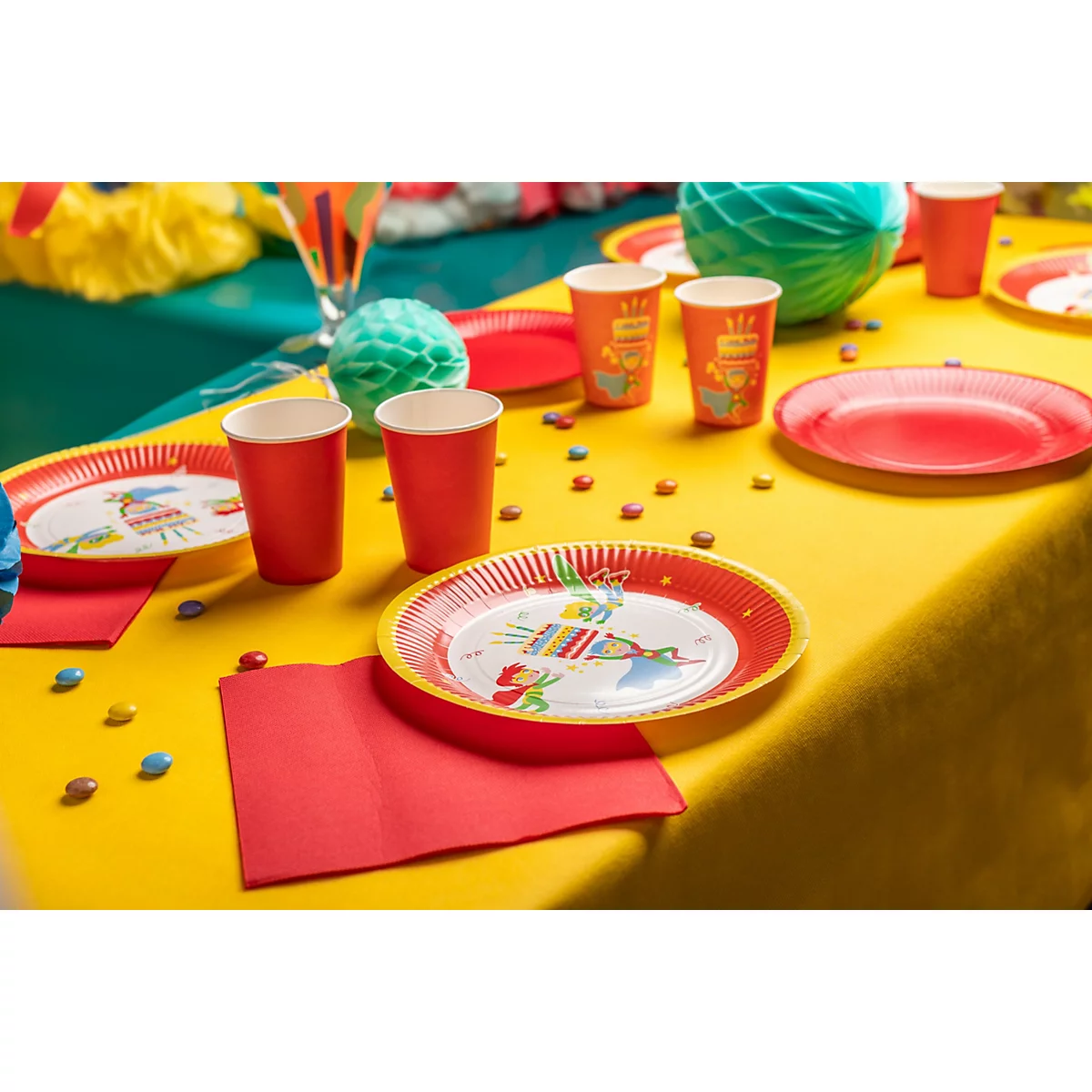 Festlich gedeckter Tisch mit Tellern, Bechern, Servietten und Süssigkeiten auf gelber Tischdecke.