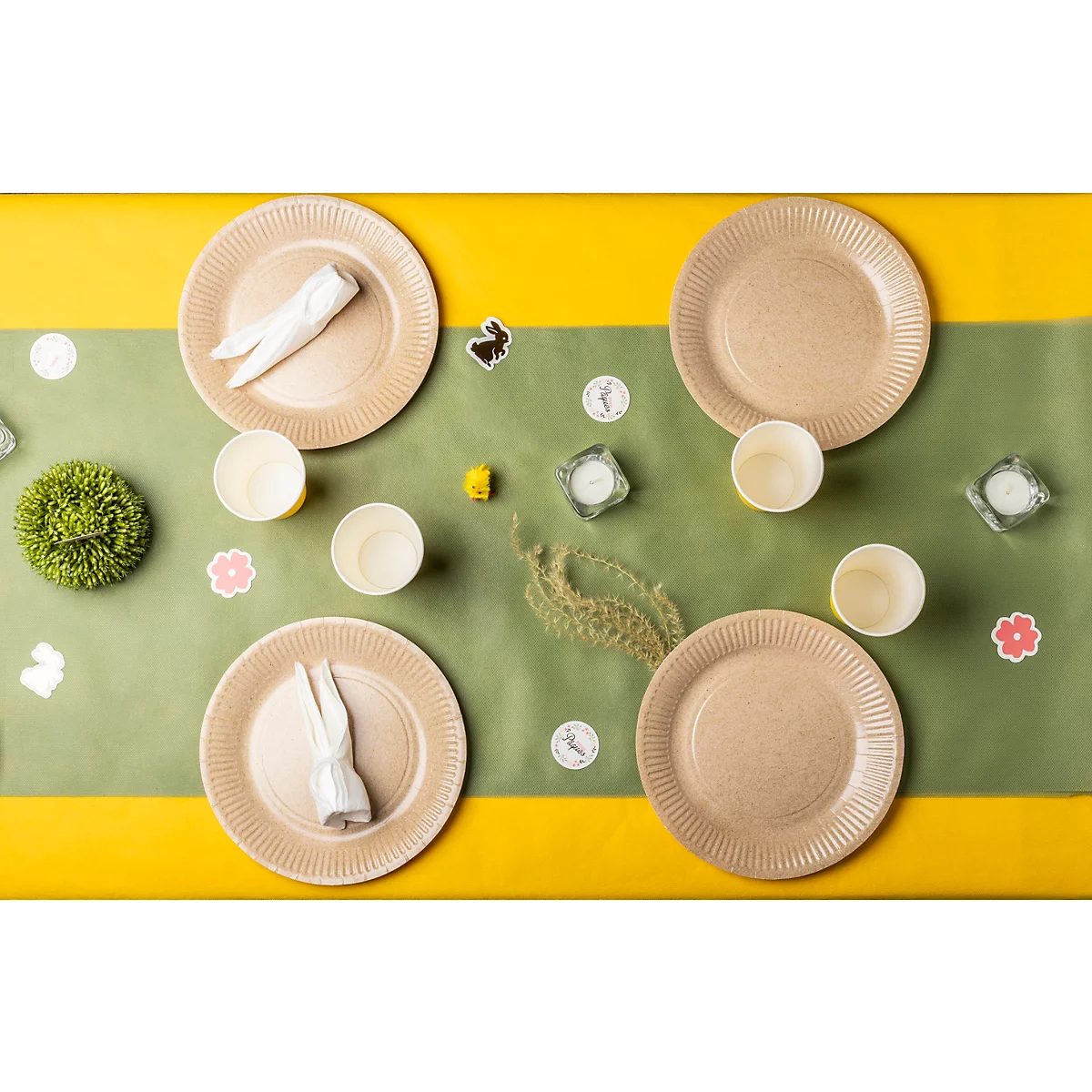 Osterdekoration mit Tellern, Tassen, Kerzen, Serviettenhasen und kleinen Blumen, auf gelb-grünem Tisch