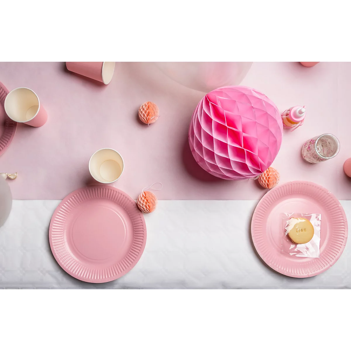 Draufsicht auf einen festlich gedeckten Tisch in Rosa. Teller, Becher und Dekorationen sind zu sehen.